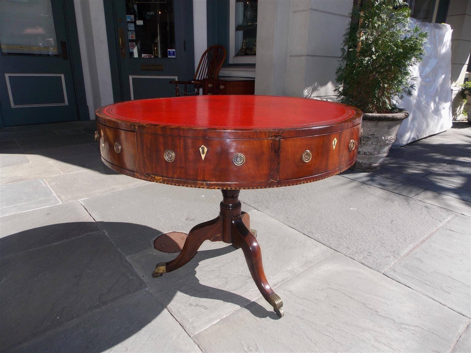 English mahogany four drawer red leather top rent table with circular swivel top, diamond bone escutcheons, checkered inlays, and terminating on a tripod base with original brass casters.  Late 18th Century