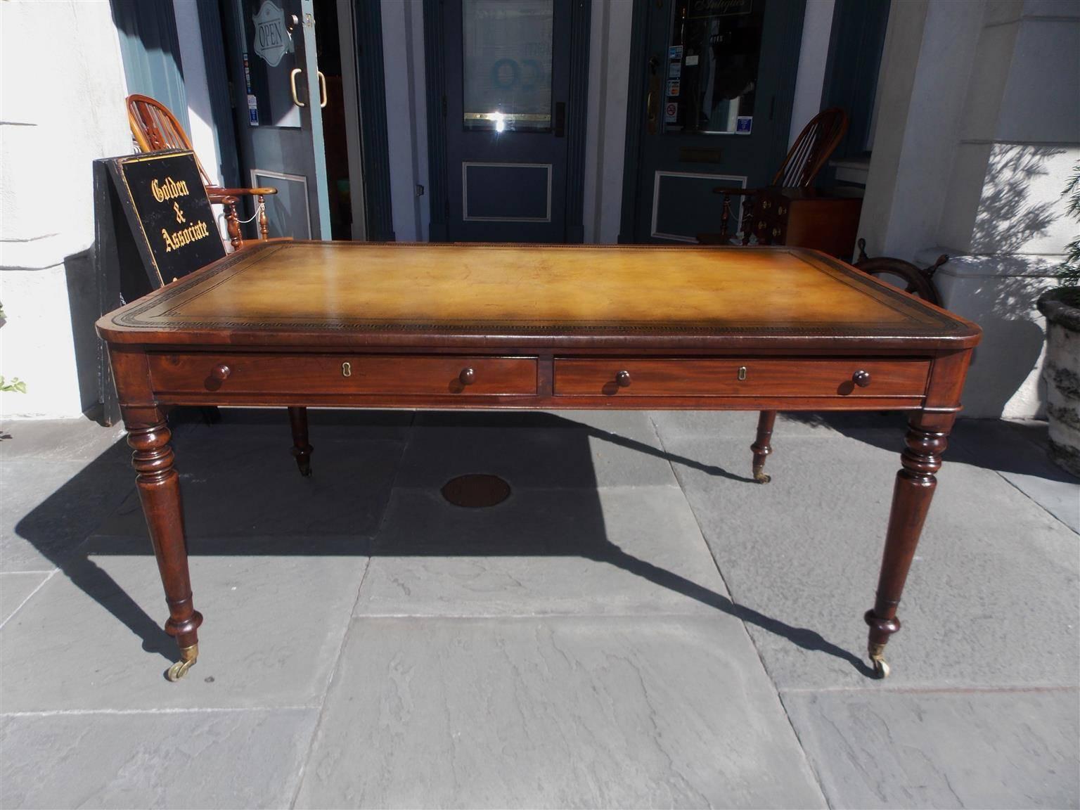 English mahogany two drawer leather top writing desk with Greek Key tooling, original wooden knobs, rounded corners, and terminating on turned bulbous ringed legs with the original brass casters.  Early 19th Century.