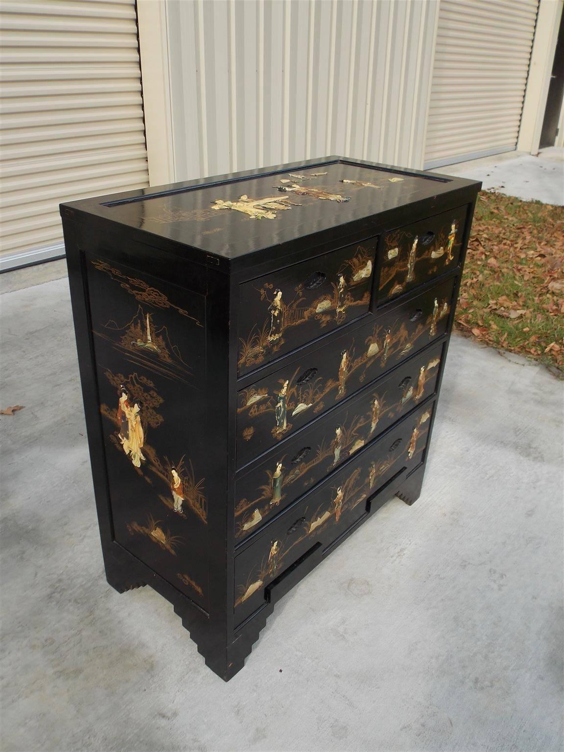 Chinese stenciled and gilt black lacquered graduated five drawer chest with decorative carved figures, landscapes, two secret lower hidden drawers, and terminating on step back carved feet.  20th Century