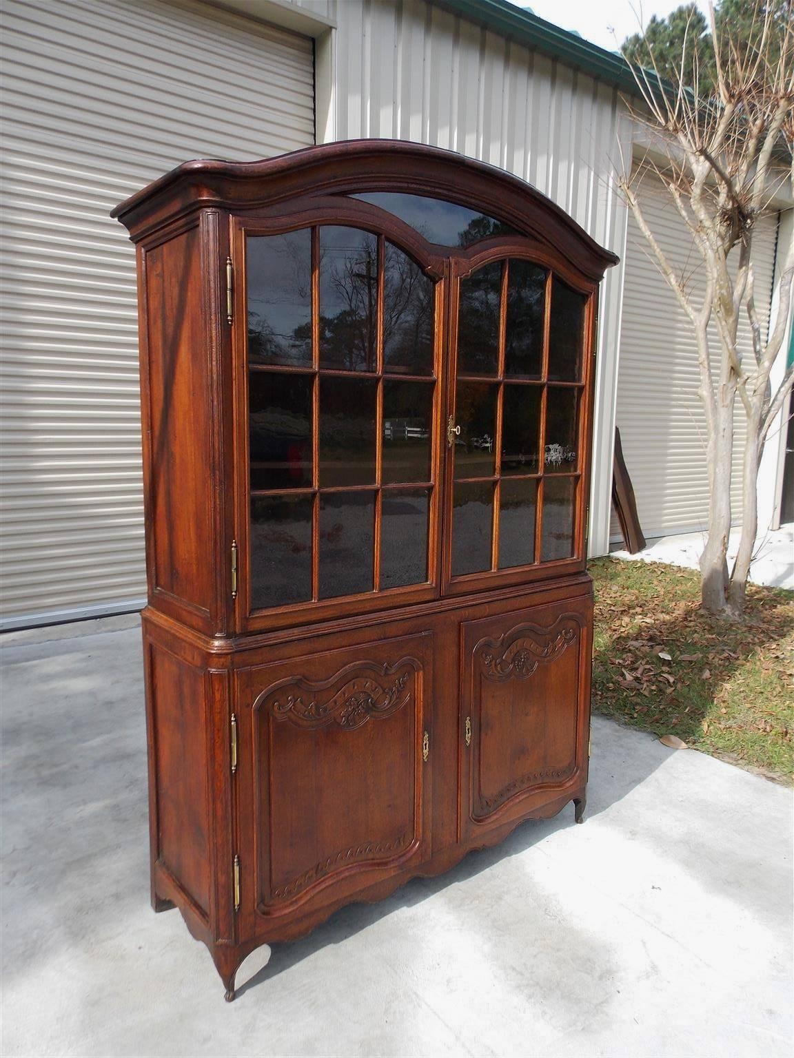 French Provincial walnut cupboard with arched dome cornice, flanking upper case glass doors with adjustable interior shelving, lower case flanking doors on the original brass hinges, hand carved exterior floral molding and terminating on the