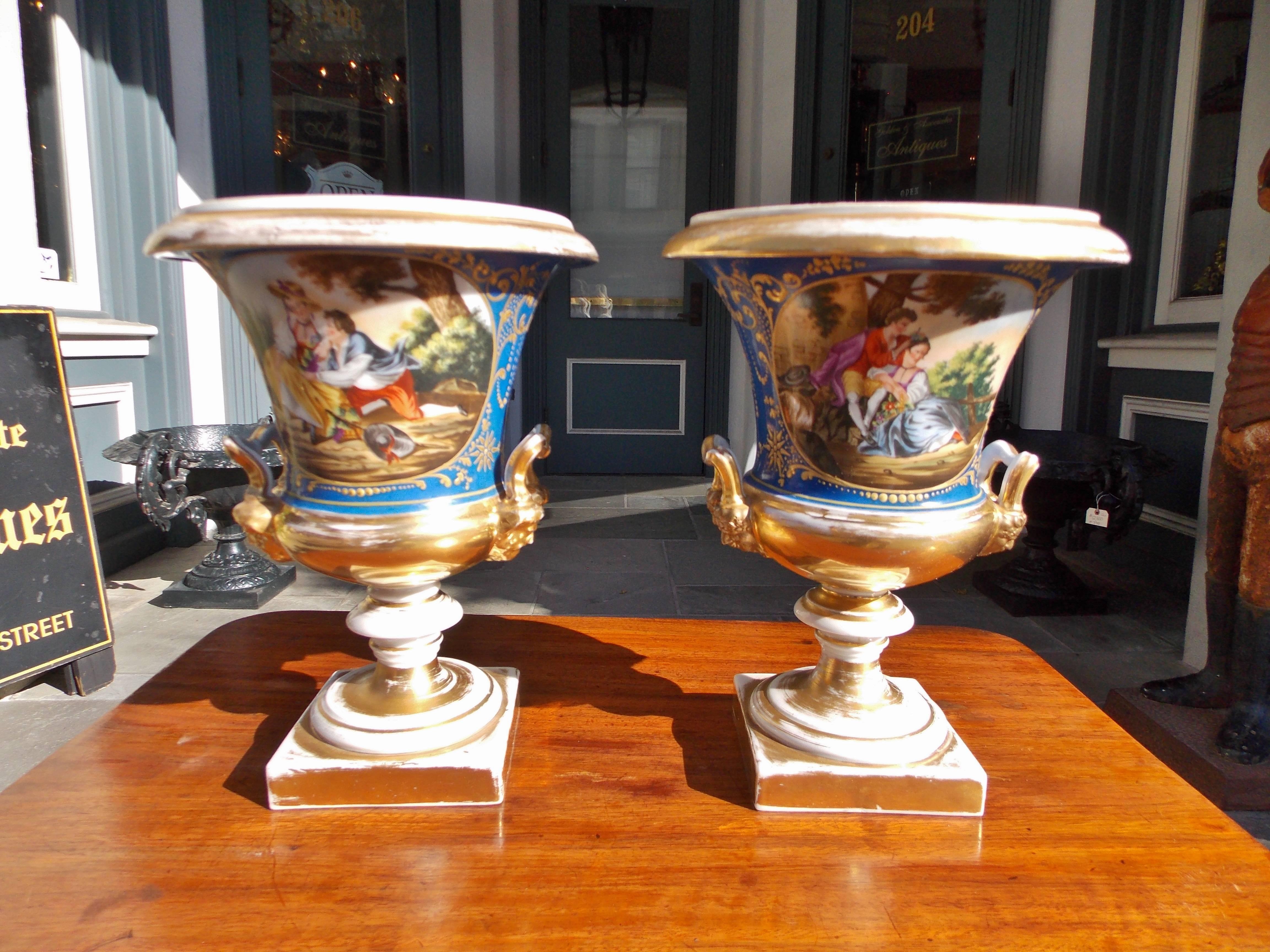 Pair of French Old Paris gilt and cobalt blue porcelain mantel urns depicting figural landscape scenes, reverse floral & filigree motif sides, figural side handles, and terminating on bulbous squared gilt plinths, Early 19th Century. 4.5