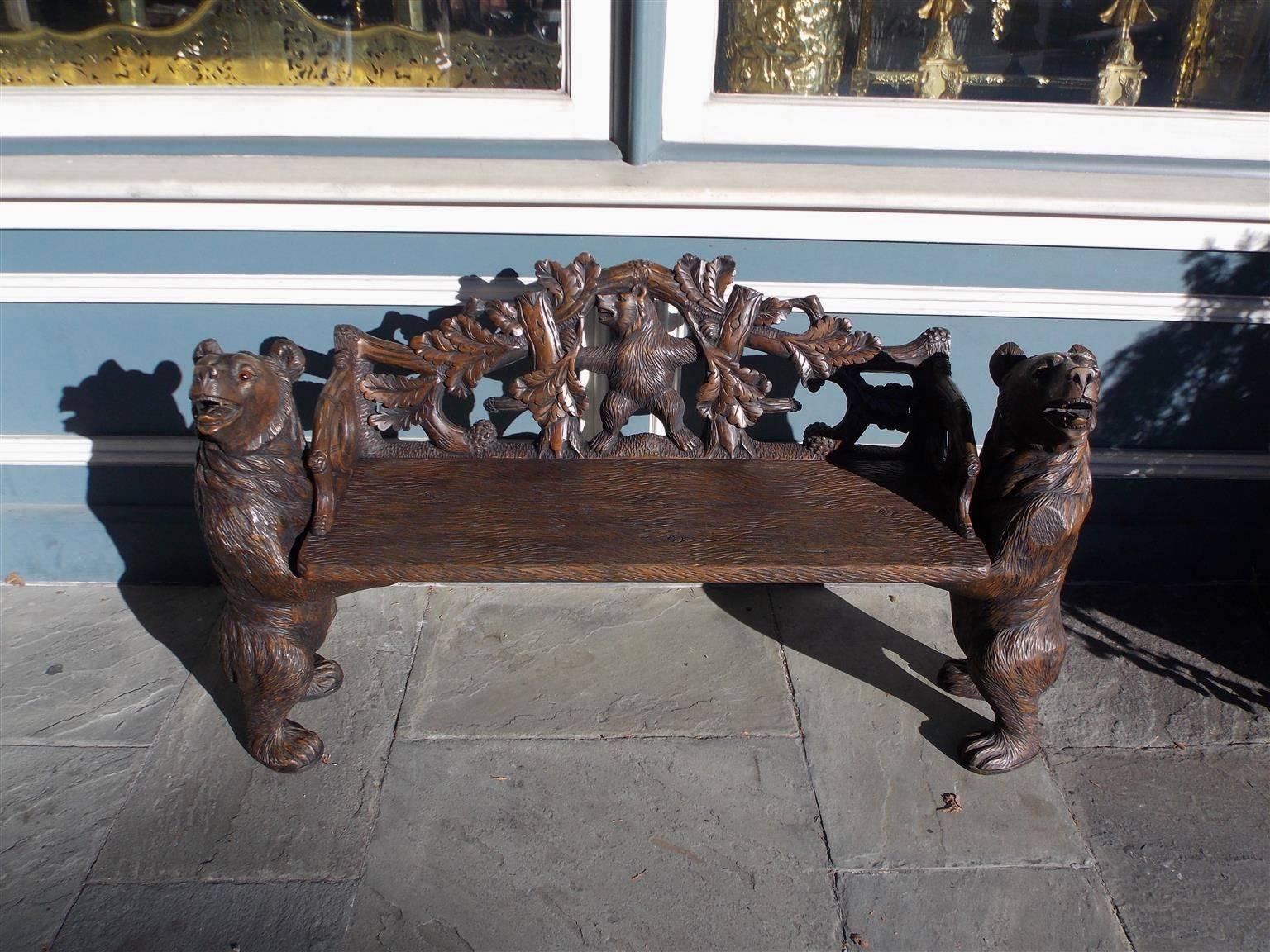 Solid walnut hand-carved black forest bear bench with carved centered standing bear, flanked by branches and oak leaves, two major standing bears with the original glass eyes, and a one board seat, Switzerland, Early 20th century. 

Many relate