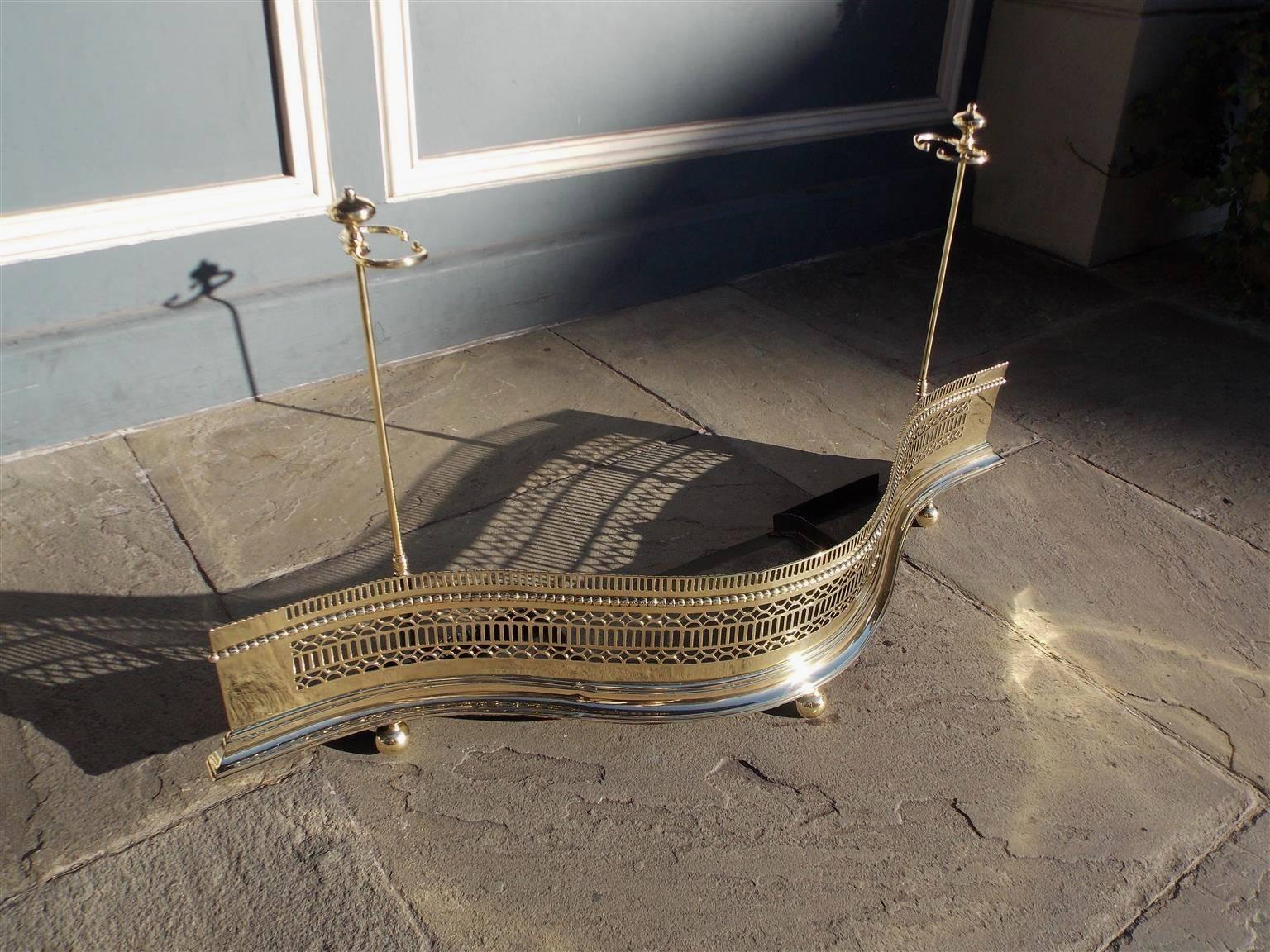 English brass serpentine fire fender with decorative pierced hand chased gallery, single row of beading, flanking side tool holders, and terminating on a molded edge base with ball feet.  Mid 18th Century.  Fender is 23