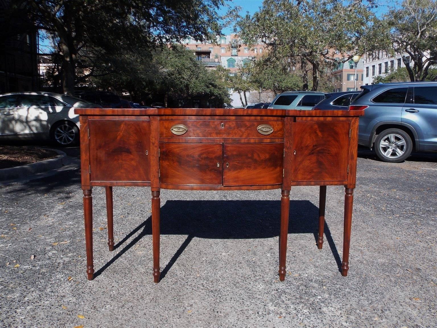 American mahogany bow front sideboard with a single drawer , flanking cabinets, lower case compartment & terminating on turned bulbous legs . Mid-Atlantic . Early 19th Century. 