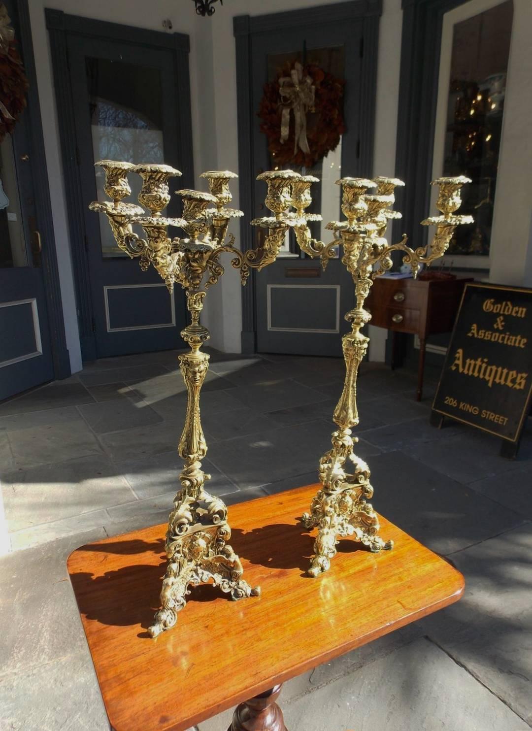 Pair of Italian bronze five-arm figural candelabras with decorative floral motif, flanking rams heads, and terminating on a tripod base with acanthus winged cherub motif. Early 19th century. Candle powered and can be electrified if desired.