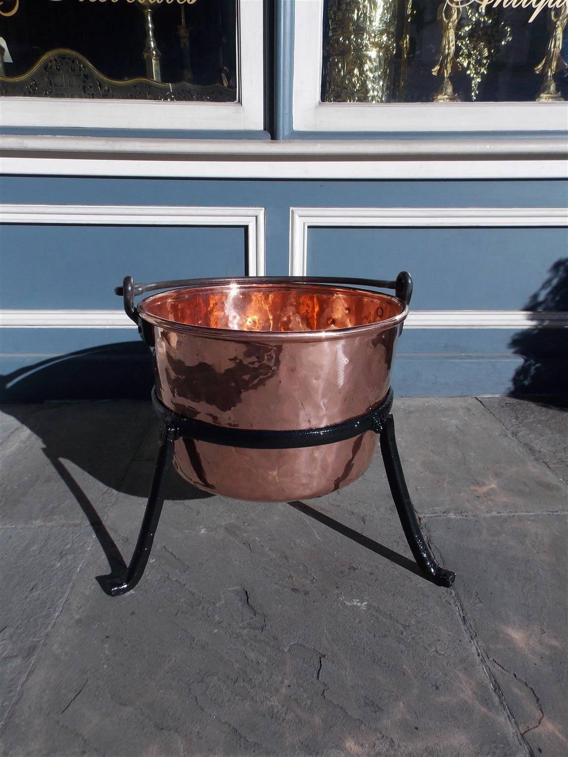 American copper and wrought iron plantation cauldron with original iron folding handle and supported by circular fitted three leg stand with stylized splayed feet. Late 18th Century. Cauldron is 36