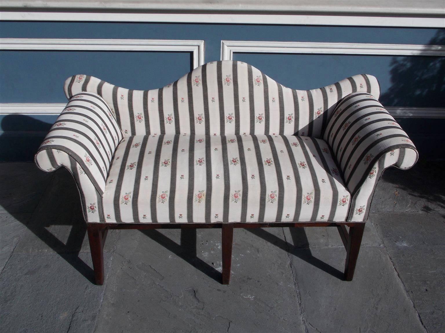 English Hepplewhite mahogany serpentine back settee with carved scrolled arms, upholstered striped silk and terminating on squared tapered legs with connecting stretchers, Late 18th century. Settee is upholstered on all sides.