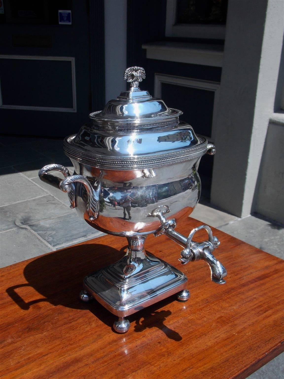 English Sheffield tea urn with floral finial, hand chased feather banding, flanking scrolled ebonized side handles, floral medallion with dolphin heads spout, and terminating on a rectangular plinth with circular bun feet, Early 19th Century.
Urn