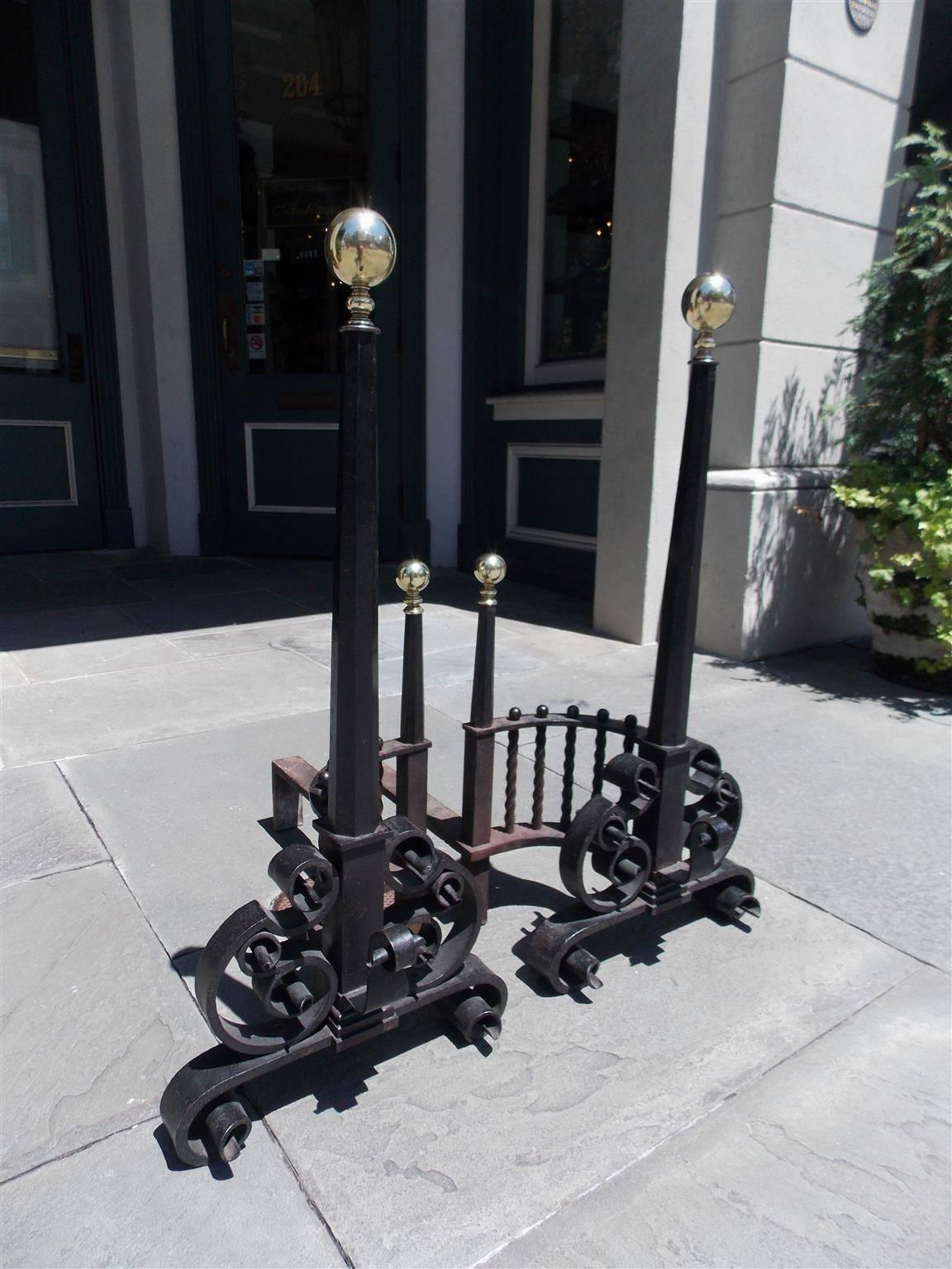 Pair of American monumental cast iron andirons with ball top finials, faceted centered columns, flanking spiral arched galleries, matching finial log stops, spit hooks, and terminating on decorative scrolled legs. Early 19th Century