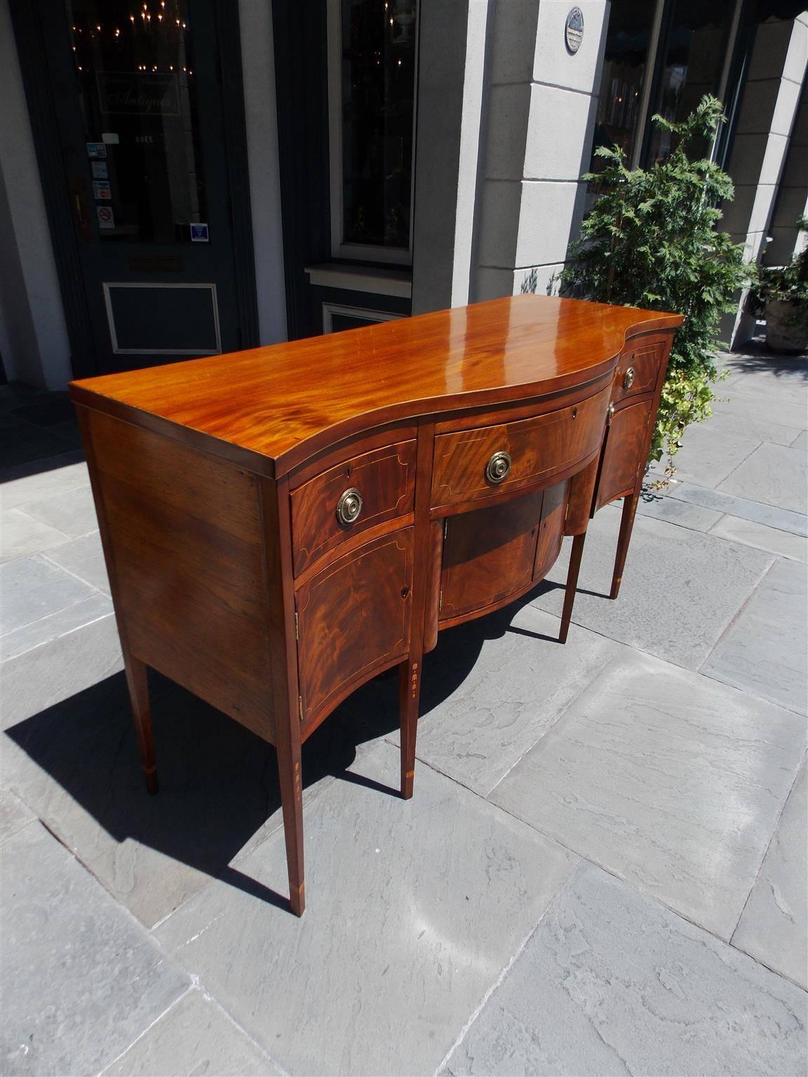 American mahogany serpentine sideboard with three upper case drawers, three lower hinged cabinets, satinwood string inlays, original brass pulls and terminating on tapered squared cuffed legs with graduated bell flower dot inlays, New York, Late