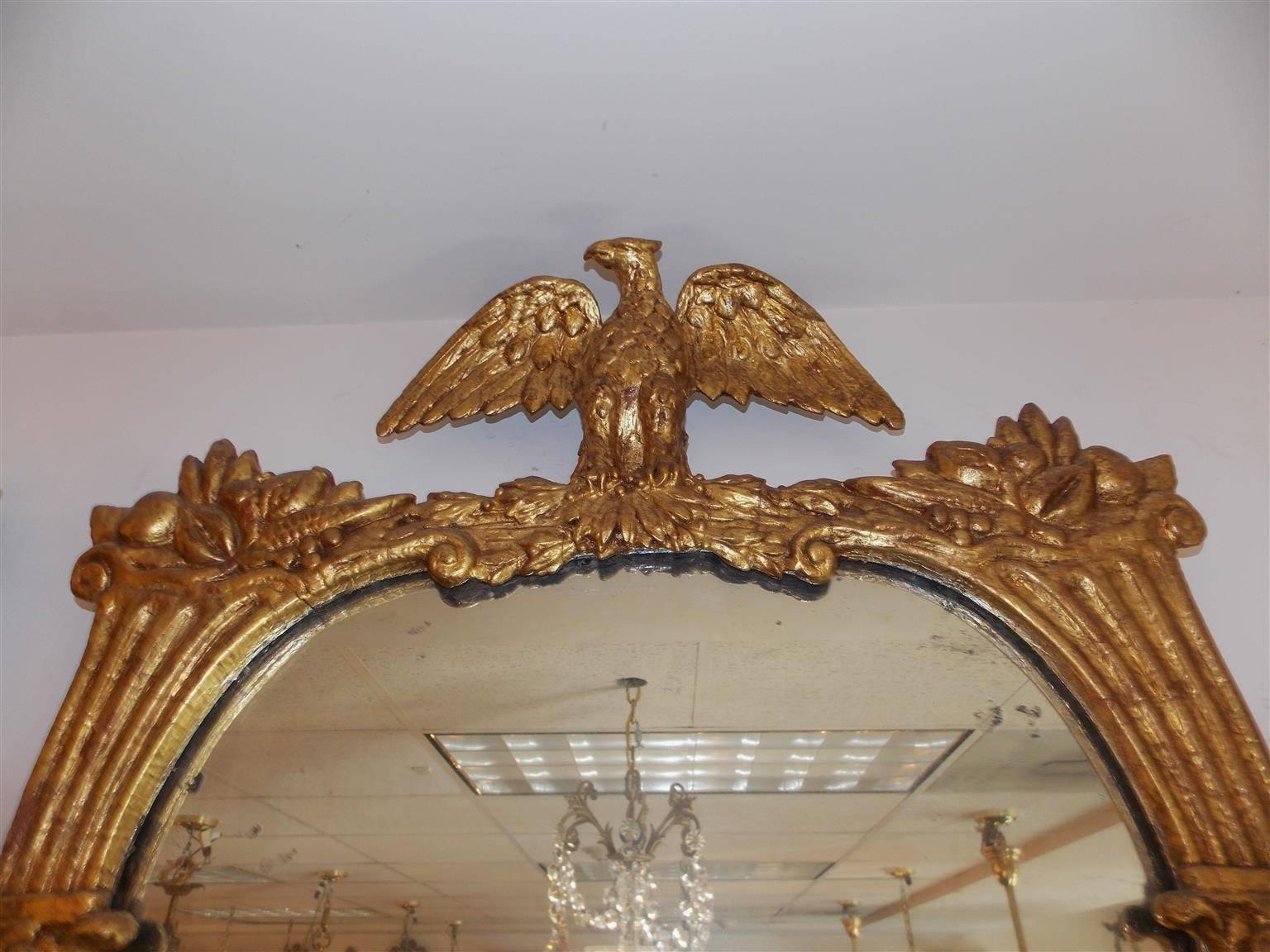 Espejo de pared americano de madera dorada tallada con cornucopias flanqueantes, águila posada a la fuga y medallones florales decorativos. El espejo conserva el cristal y la trasera de madera originales. Mediados del siglo XIX.