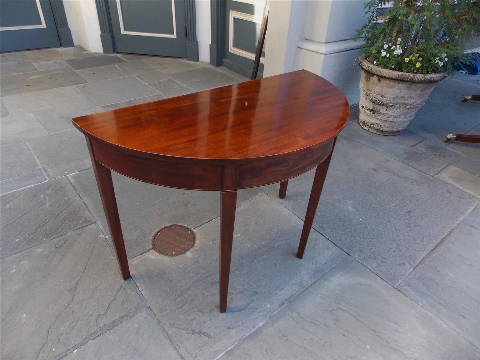 American Charleston mahogany demilune one board top console with satinwood and ebony string inlaid skirt and terminating on tapered squared legs, Late 18th Century.