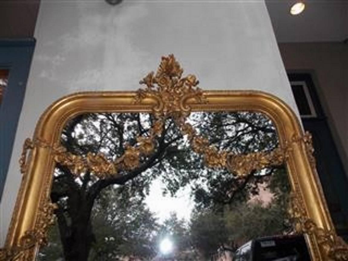 French gold gilt and gesso wall mirror with centered floral cartouche, decorative floral swags, interior bead work, and resting on a carved molded edge. Mirror retains the original glass and wood backing. Early 19th century.
