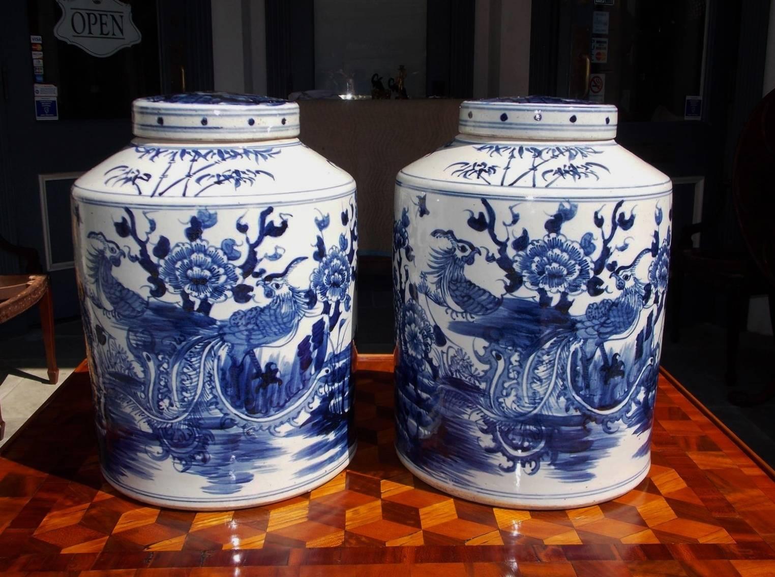 Pair of Chinese porcelain glazed blue and white temple jars with hand-painted parrots perched in trees, decorative flowers, and a running stream. Lids are removable and jars were used to store food and perishable goods, 20th century.