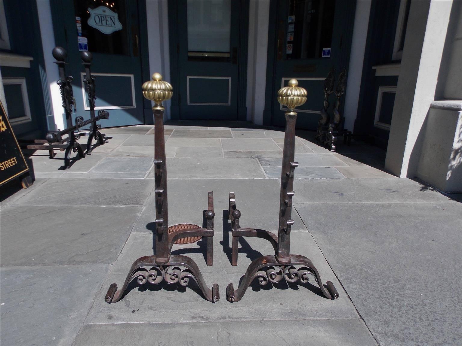 Pair of English wrought iron and brass melon top andirons with hand chased finials, flanking spit hooks, matching ball log stops, and terminating on decorative scrolled stylized legs. Early 19th century.