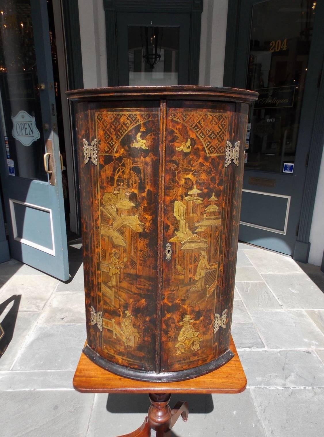 English chinoiserie hanging corner cupboard with a carved upper molded edge, figural and pagoda landscape scenes, original four butterfly hinges, original locking mechanism, three fitted interior shelves and terminating on a lower carved molded