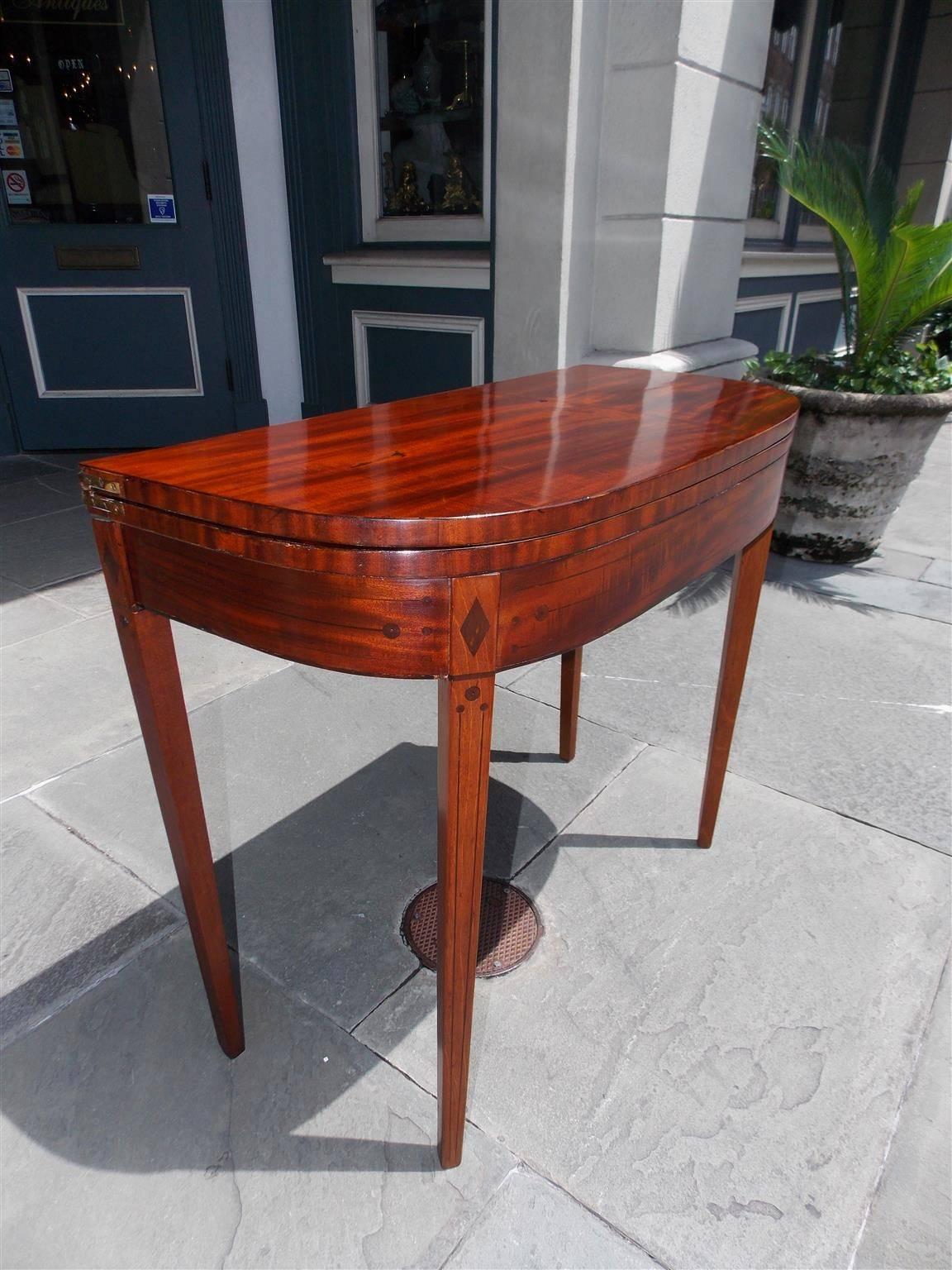 English mahogany demilune hinged card table with interior baize, ebonized string and diamond shaped inlay, supporting double gate legs, and terminating on the original squared tapered legs, Late 18th century 
Card table is 17 deep closed and 33.5