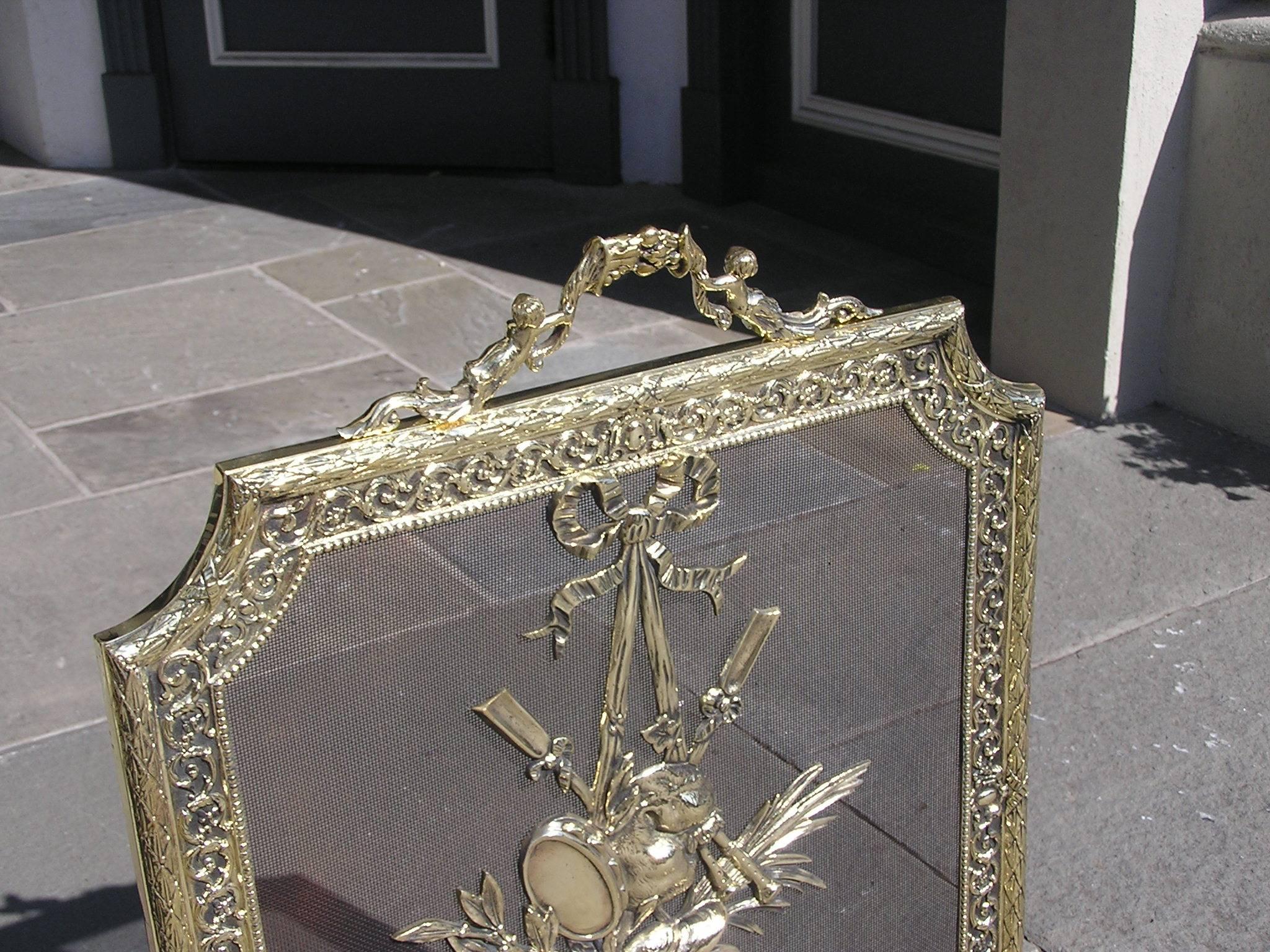 French brass freestanding fire place screen with a figural cornucopia scrolled handle, centered musical and ivy ribbon medallion, foliage scrolled beaded border with flanking lower corner rosettes, and terminating on four scrolled beaded acanthus