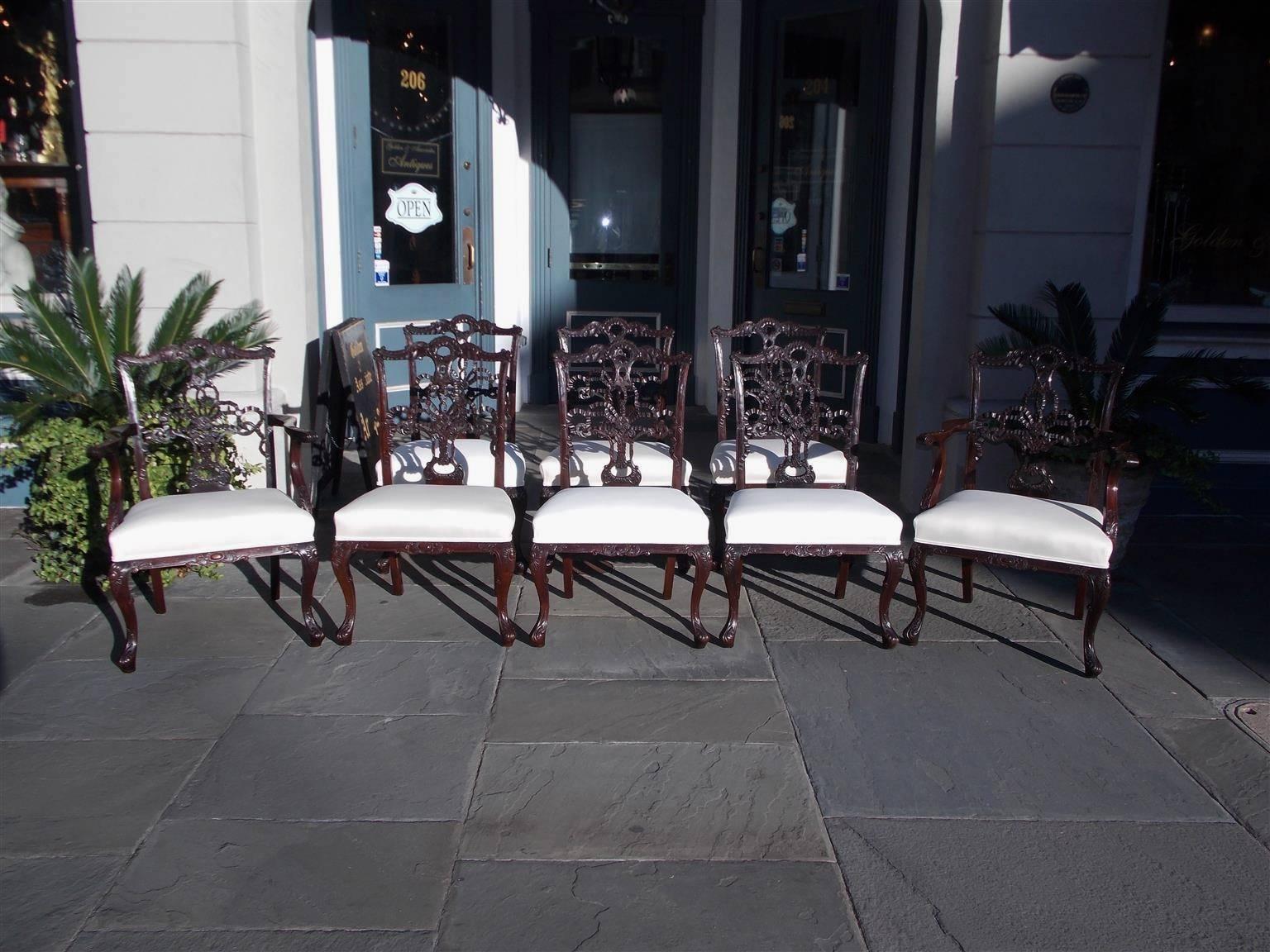 Set of eight English Chippendale mahogany dining room chairs with a serpentine carved acanthus and ribbon cresting rail, rolled foliage ears, molded edge stiles, ornate carved ribbon splat backs, gadrooned shoes, scrolled acanthus arms, upholstered