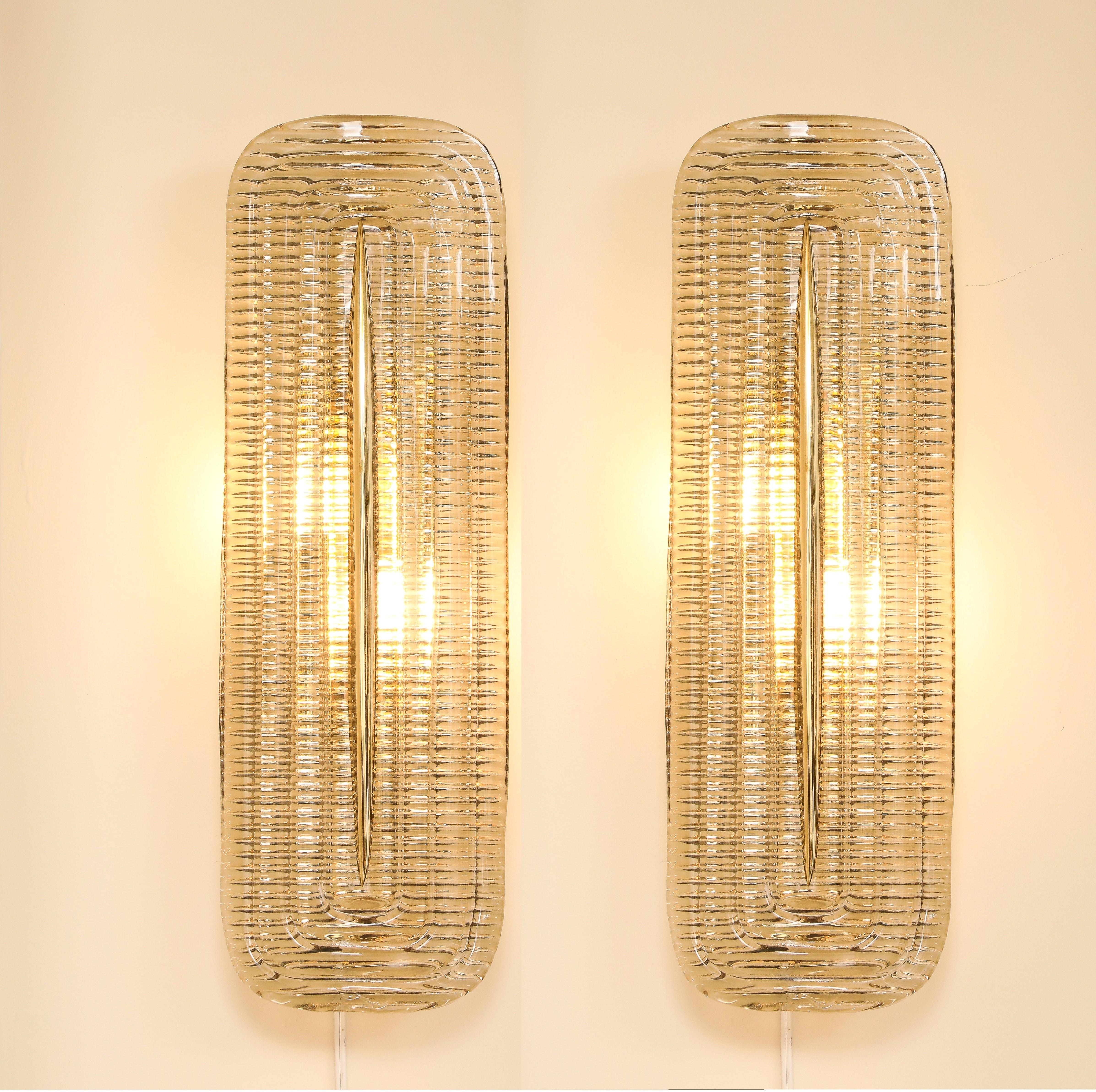 Paire d'appliques en verre clair de Murano et en laiton, fabriquées à la main, Italie, 2025. Élégante et raffinée, cette paire d'appliques murales a été méticuleusement fabriquée à la main à Venise, en Italie, en utilisant les techniques