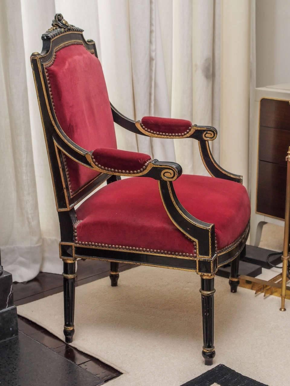 Elegant and timeless pair of ebonized (black) French armchairs with gilt details throughout; red velvet upholstery with brass nailheads.