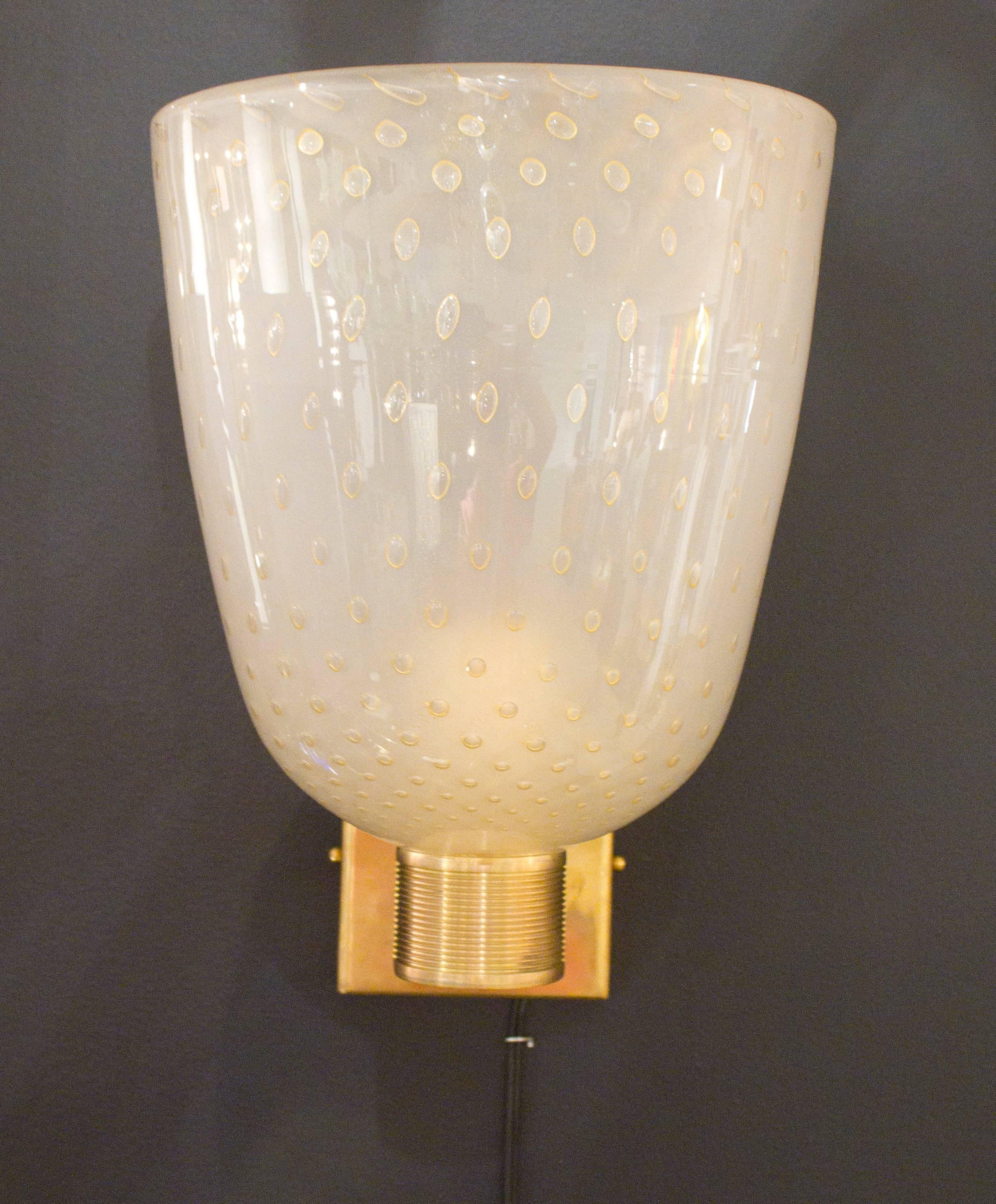 Pair of Italian Murano “pulegoso” ivory glass and brass sconces. Each brass structure holds a beautiful handblown glass cup consisting of ivory colored glass infused with 23-karat gold flecks, giving them a wonderfully warm glow. The glass was