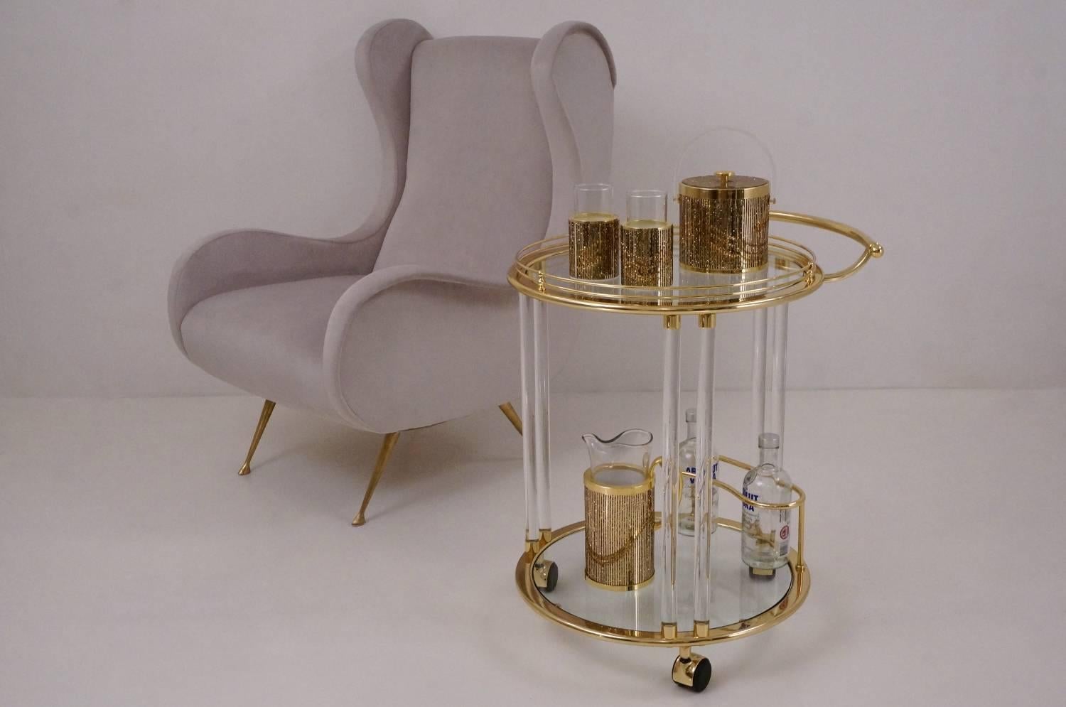 Vintage glass, brass, and lucite bar cart or trolley manufactured by Orsenigo in Milan, Italy, circa 1980. Top and bottom round glass shelves fit into brass frames. Each glass shelf is suspended by double lucite columns. Brass push btop shelf and