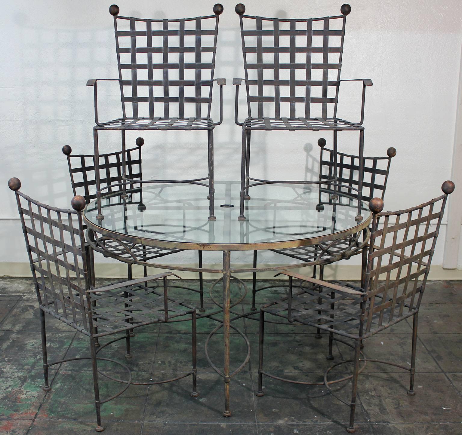 Modernist outdoor or patio dining table and set of six chairs in all original condition designed by Mario Papperzini for John Salterini. Made of iron with applied patina. Retains original thick glass top with center umbrella hole. Minor signs of age