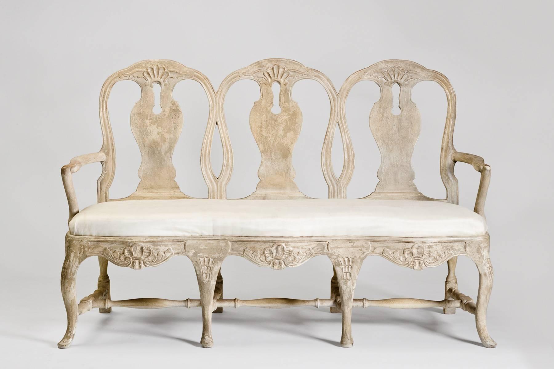 Beautiful Tara Shaw Maison Reproduction Swedish Rococo hand carved and painted wooden bench with upholstered seat. Beautiful patina and distressed look to age the wood. New Construction and material. Fabric is upholstered in off-white color that is