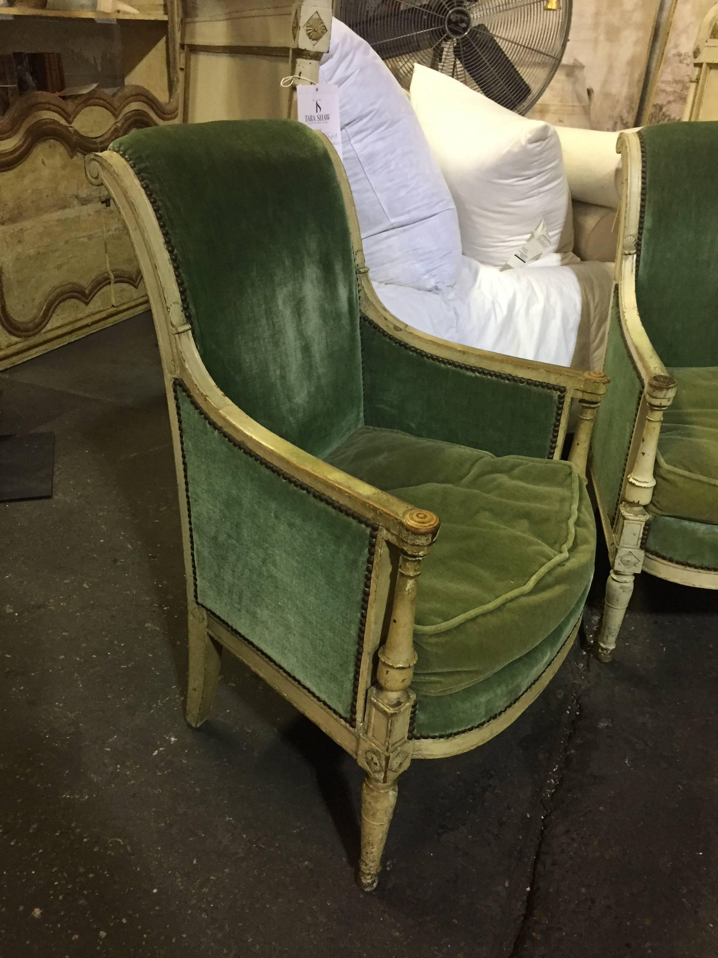 This pair of 19th Century Bergeres features a charming white patina, delicate carvings, and luxe green upholstery.