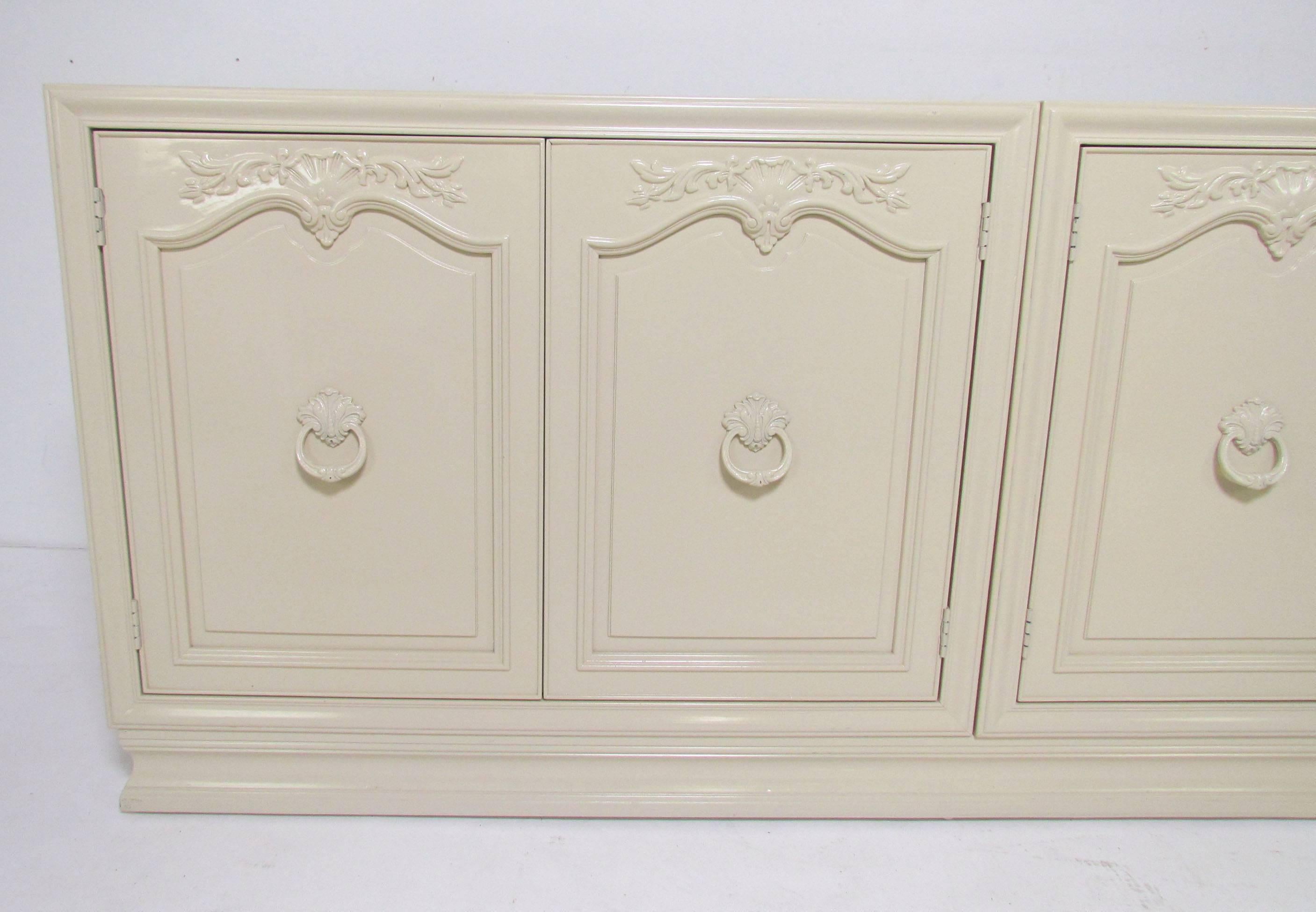 Credenza in ivory lacquer by Henredon, circa 1970s. Two matching cabinets rest side by side on a plinth base. Identical interiors feature an adjustable shelf and silverware drawers lined with anti-tarnish flannels.