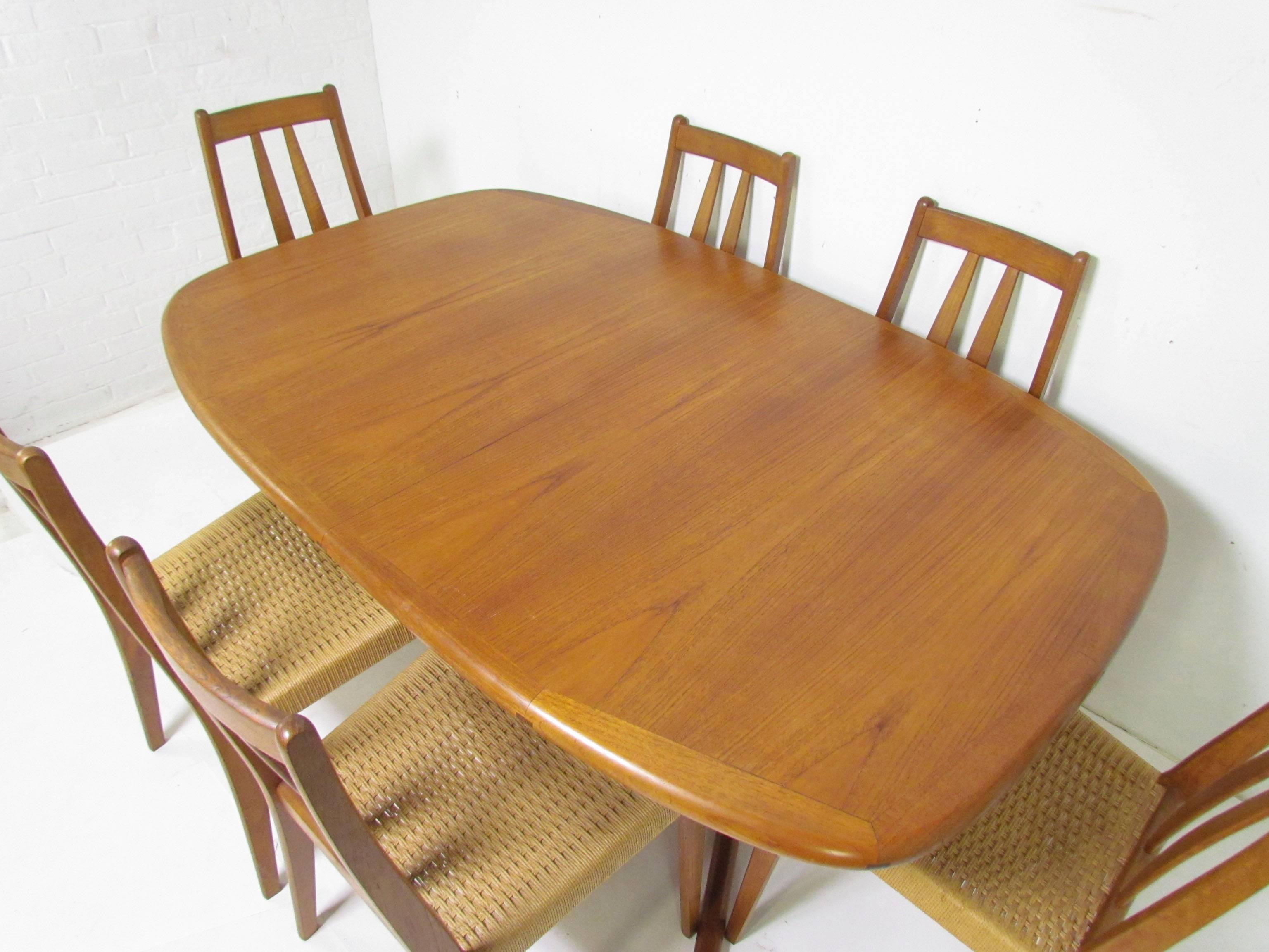 Mid-Century oval dining table in teak by Dyrlund, Denmark, with six high back teak dining chairs with original woven cord seats. Table includes two extension leaves that can be stored inside the table.

Table measures 104