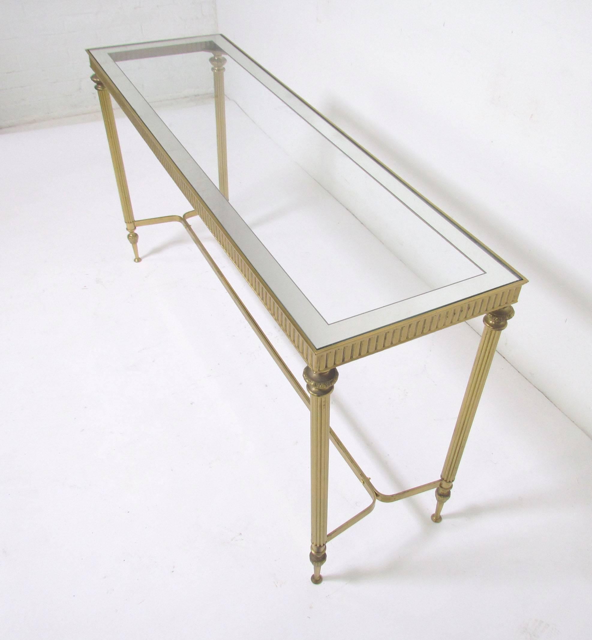Classic Hollywood Regency style brass console table with reeded leg detail, circa 1960s. Glass top features mirrored edge banding. Most likely Italian.