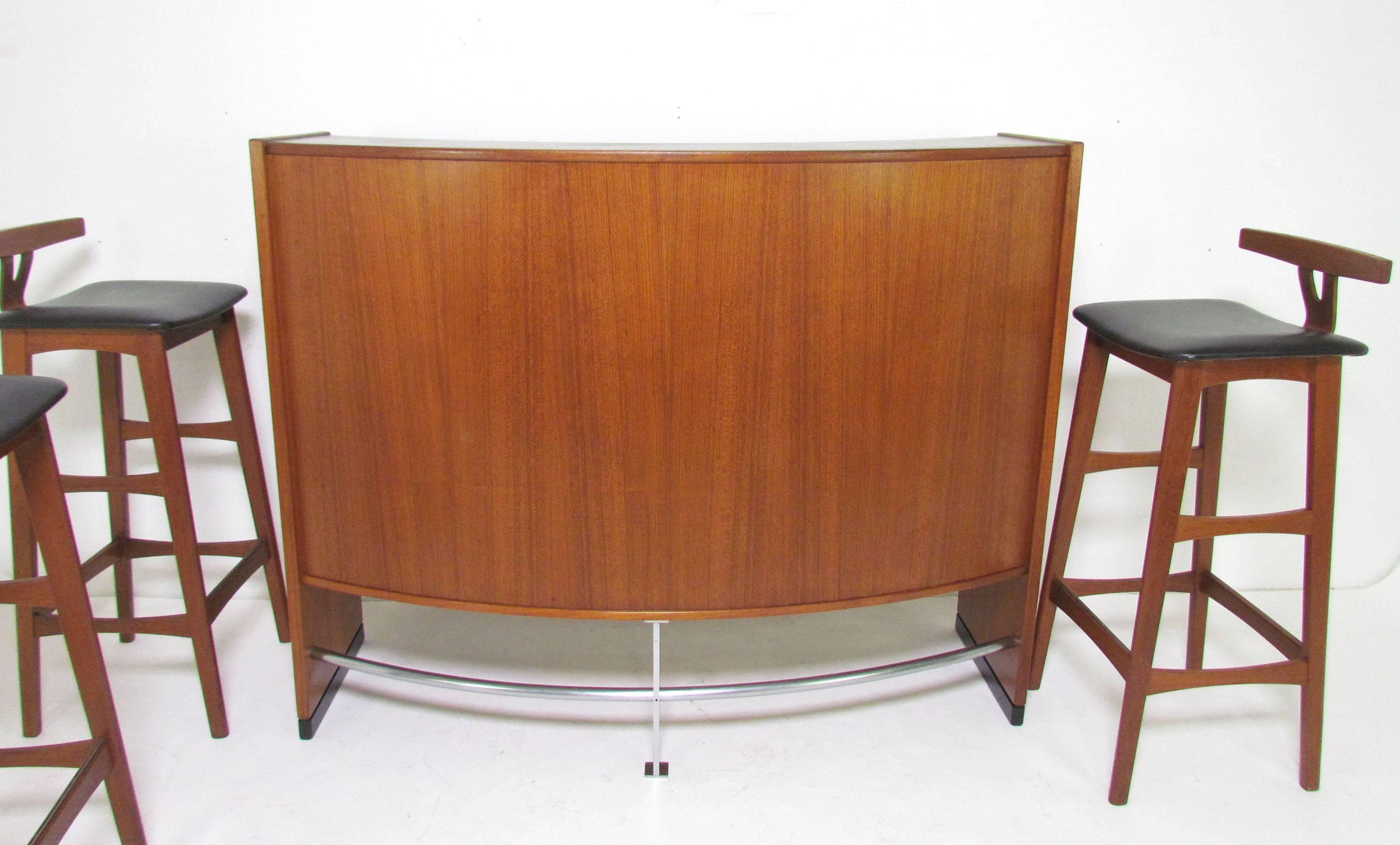 Bow front teak bar and three bar stools designed by Erik Buck for Dyrlund, Denmark, circa 1970s. Multiple compartments for storage of liquor bottles, linoleum top work surface for mixing and serving of beverages. The bar is double-sided and can be