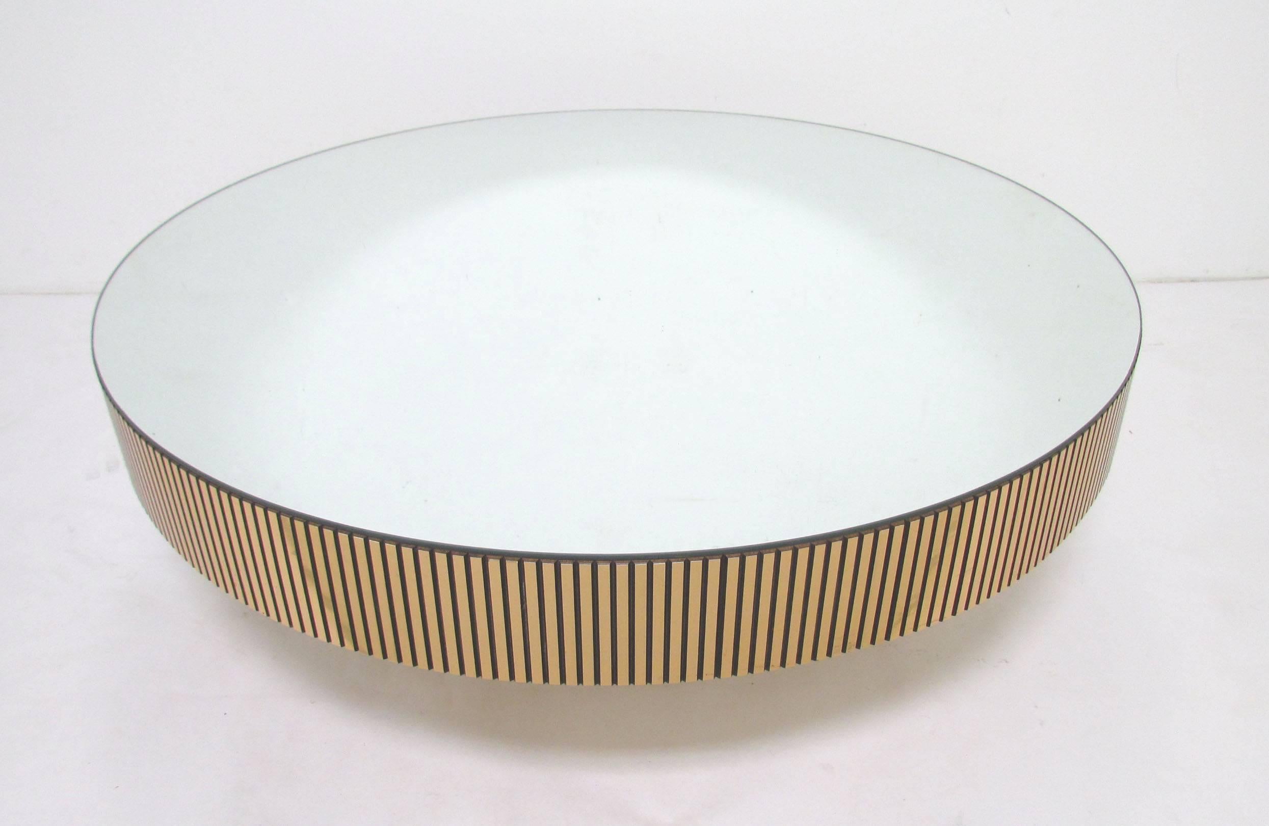 Mid-Century full-circle coffee table with mirrored top, and contrasting sides and pedestal base consisting of ribbed brass-toned strips. Attributed to Ello, circa 1970s.