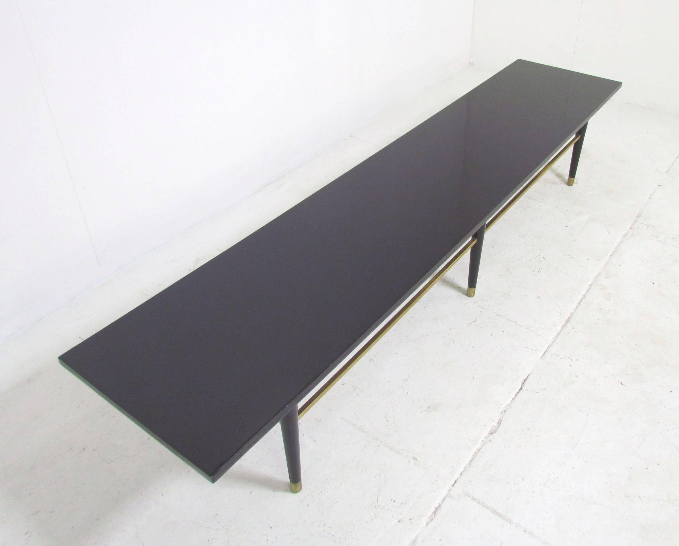 Mid-Century American modern coffee table in the manner of Paul McCobb. High gloss black lacquer with brass stretchers and feet. Generously proportioned at 84" long (7' 2").