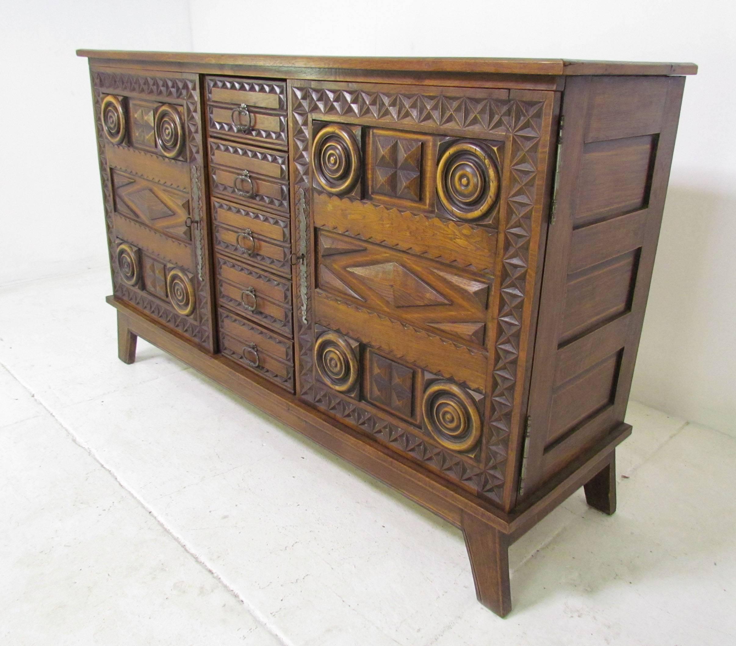 A striking server cabinet in hand-carved oak with geometric decorations. Five center drawers flanked by two doors with shelving space. With original skeleton keys which also function as pulls for the doors.