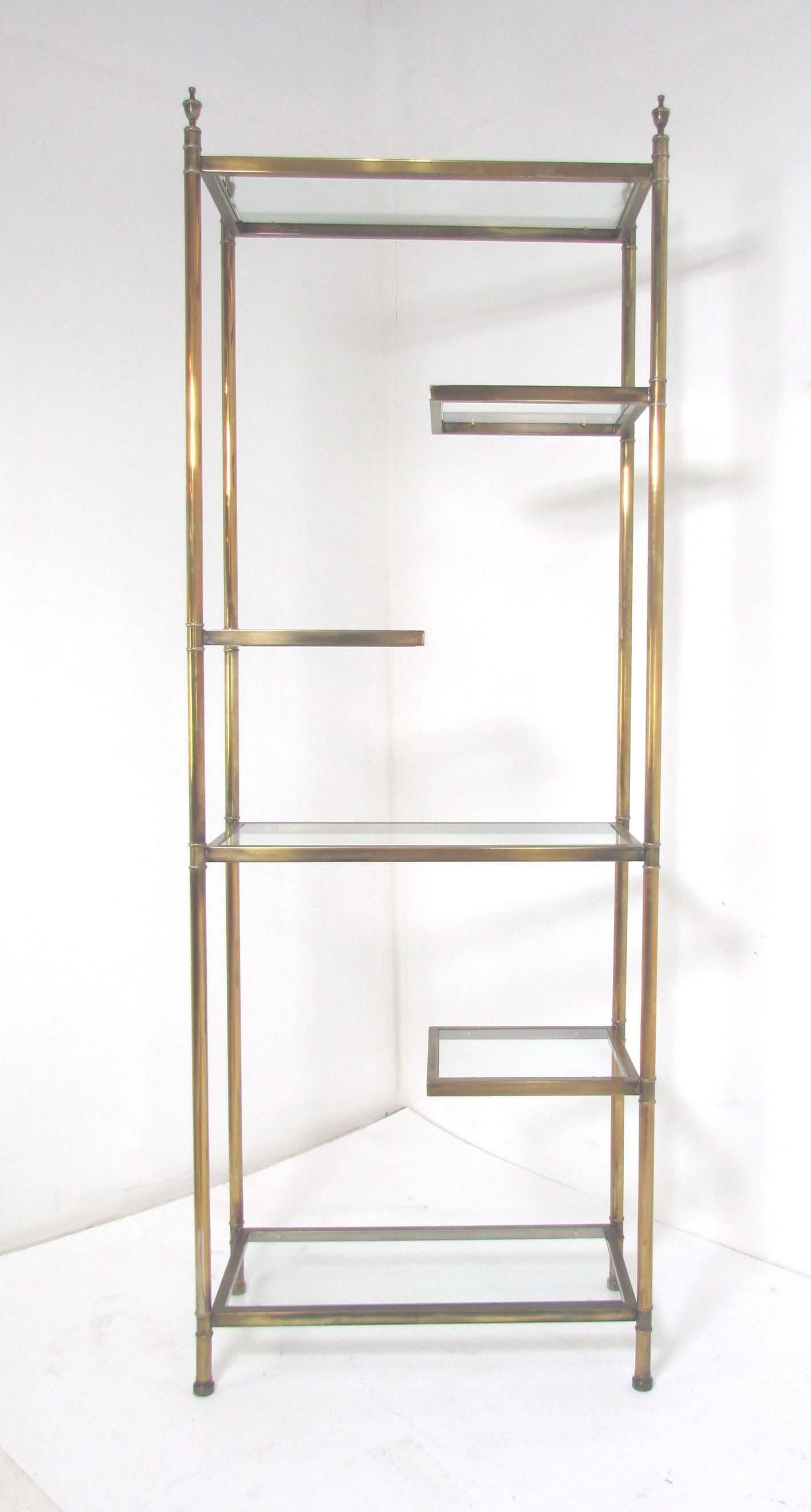 Elegant étagère in brass with glass shelves, with unusual stepped cantilevered shelf design, circa 1950s. Unmarked, but reminiscent of Mastercraft or Maison Jansen designs.
