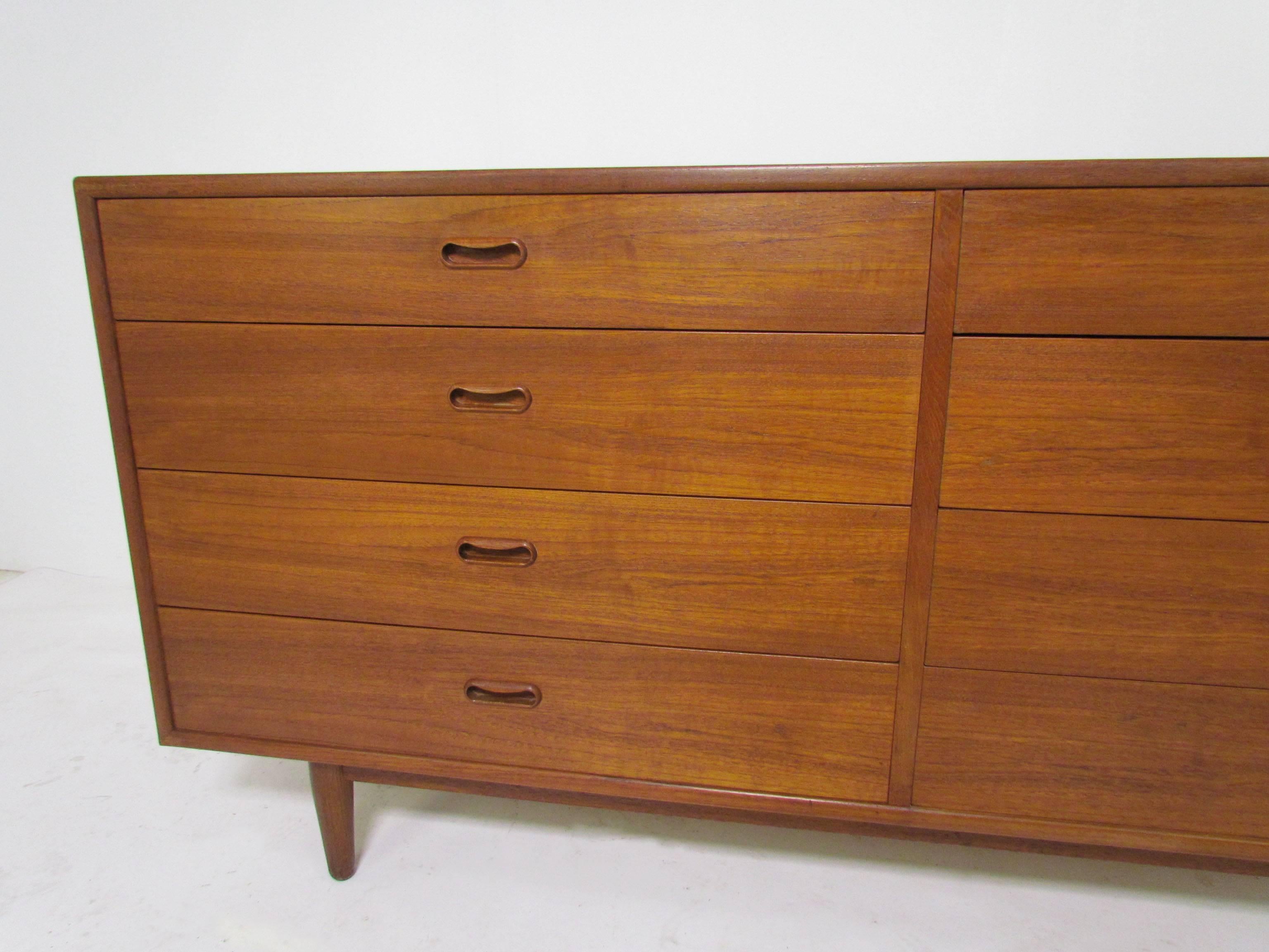 Danish teak eight-drawer dresser featuring a sleek low profile, bookmatched grain, and carved inset pulls, circa 1960s. This has a finished back so can float in a room if desired. Retailed at Spivack Furniture, New York.