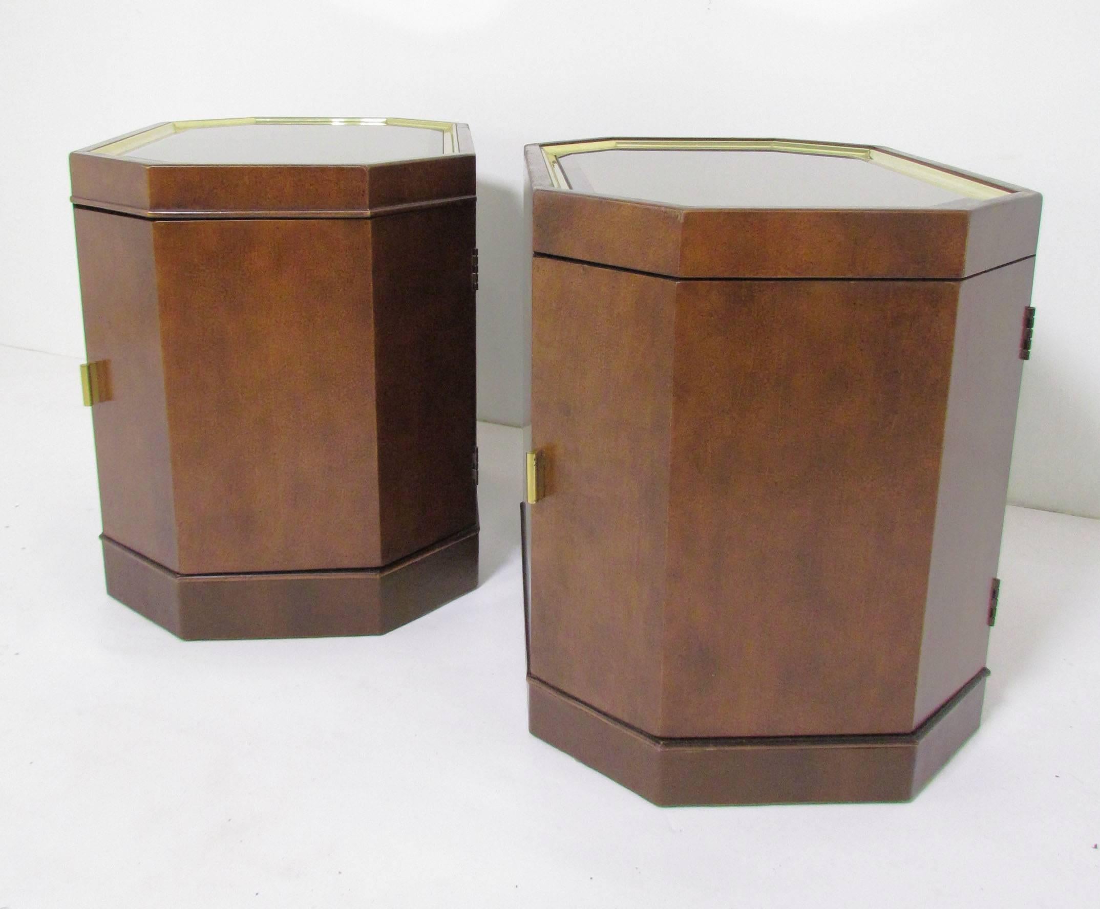 Pair of octagonal end tables with leather wrapped bases, brass handles and smoked mirrored tops, circa 1960s, in the manner of Harvey Probber.

Slight variance in design in that one has a small band of wood trim above the door. This minor