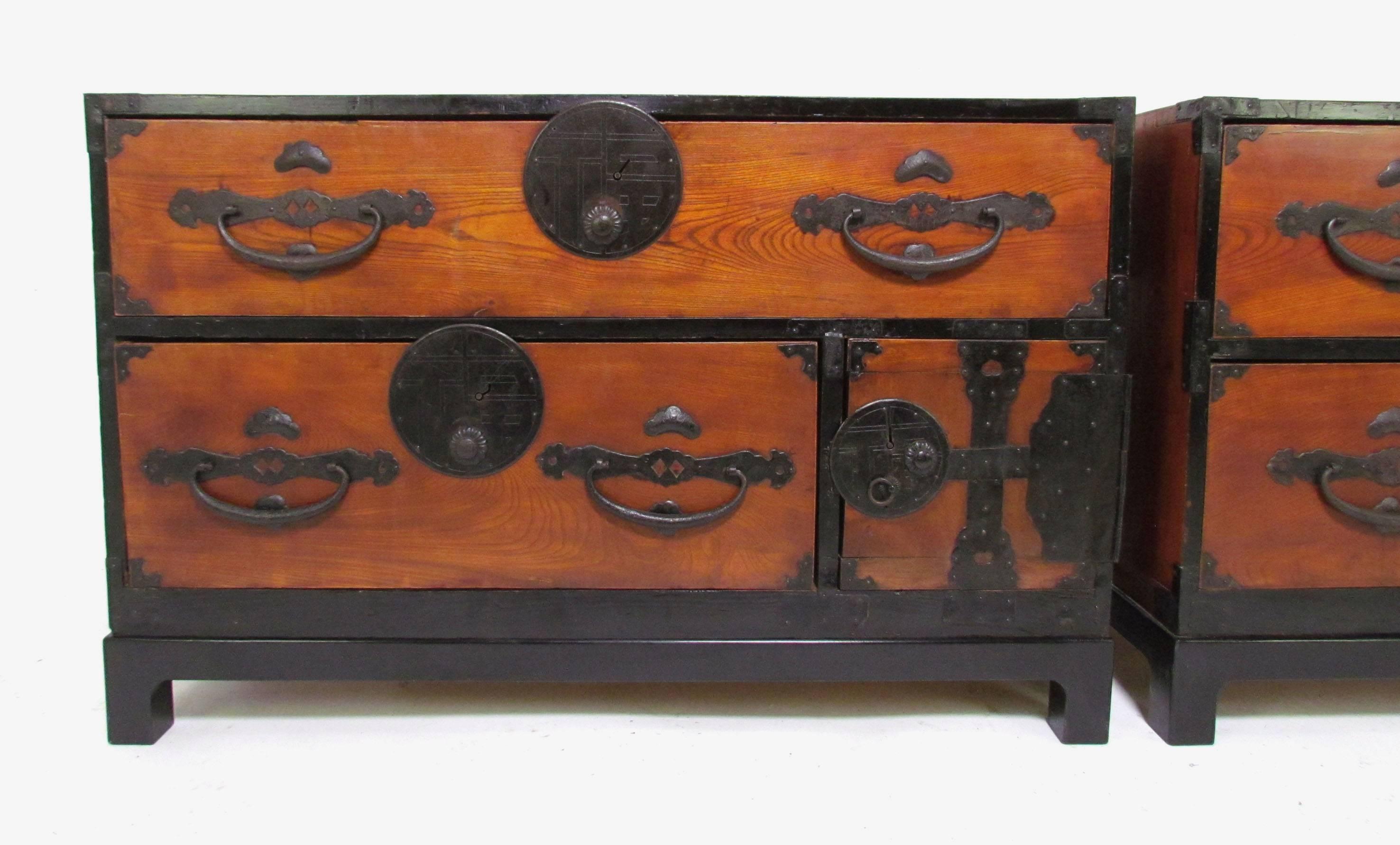 Pair of antique late 19th century Meiji period lacquered Tansu chests. Originally a two part stacking chest, these were modified in the mid-20th Century as flanking chests and fitted with custom ebonized bases. Intricate hand-forged iron hardware