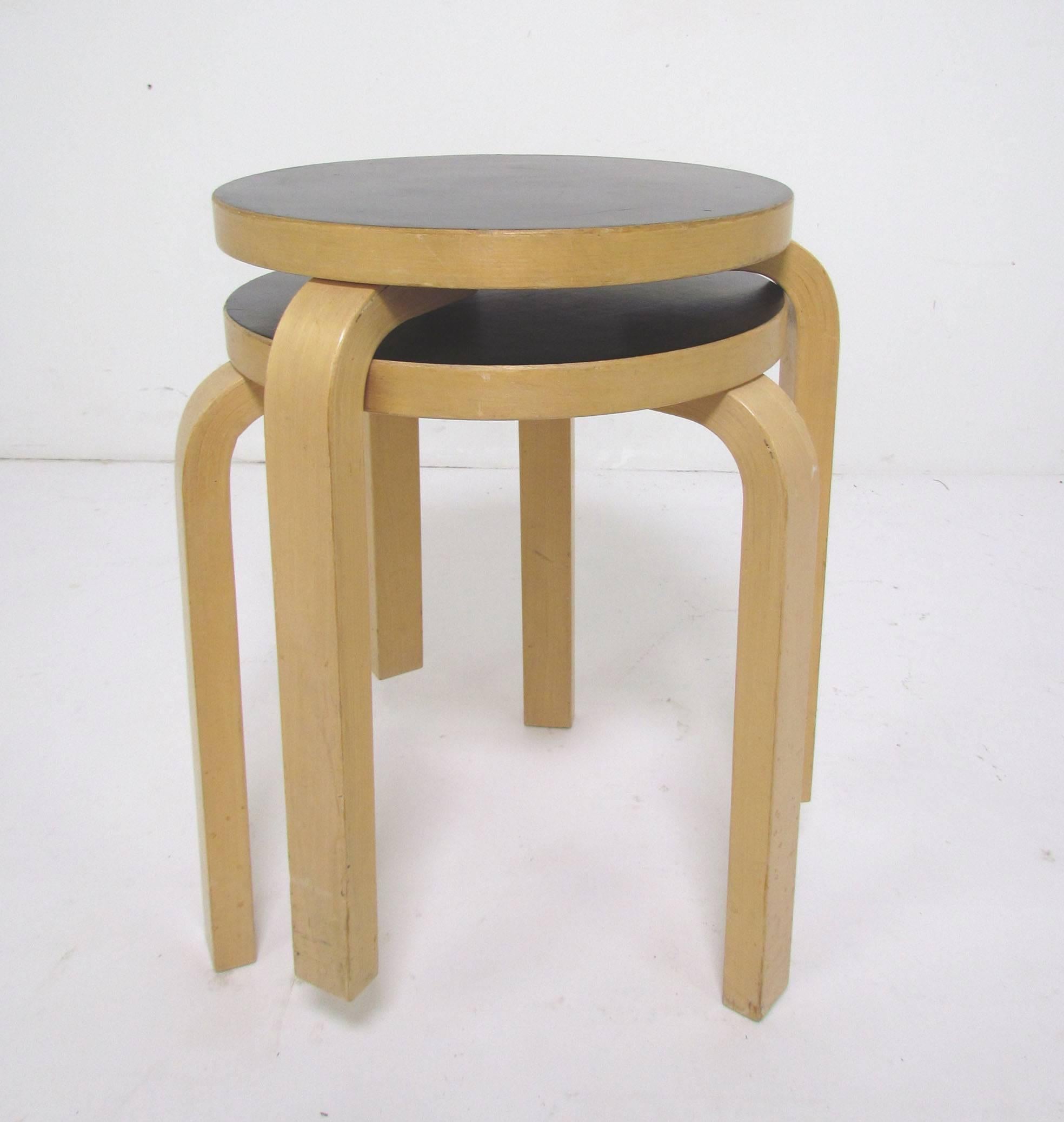 Pair of iconic three legged stacking stools in bent ply birch with inset linoleum tops, designed by Alvar Aalto in the 1930s, this pair dates to the mid-1960s.  Can also serve as occasional side tables.

Surface diameter  13.5