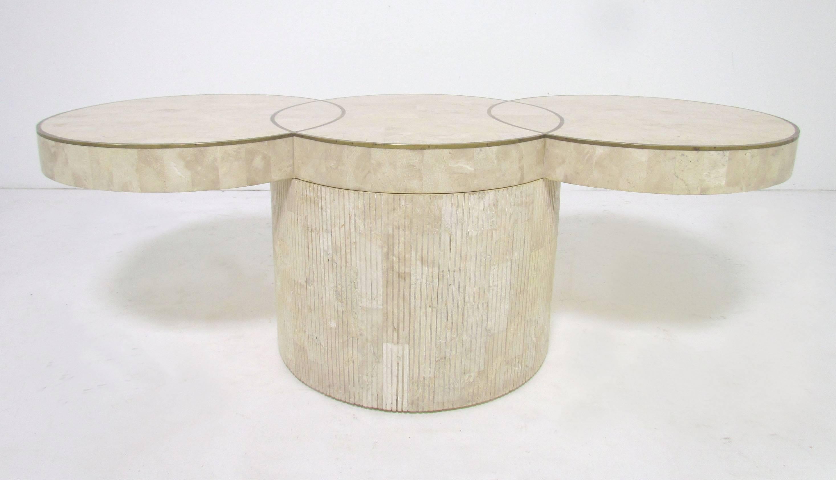 Cocktail table with tessellated fossil stone top of three conjoined disks inlaid with a brass trim border, and carved reeded fossil stone base. Unmarked, but bears all the design elements associated with Maitland Smith.