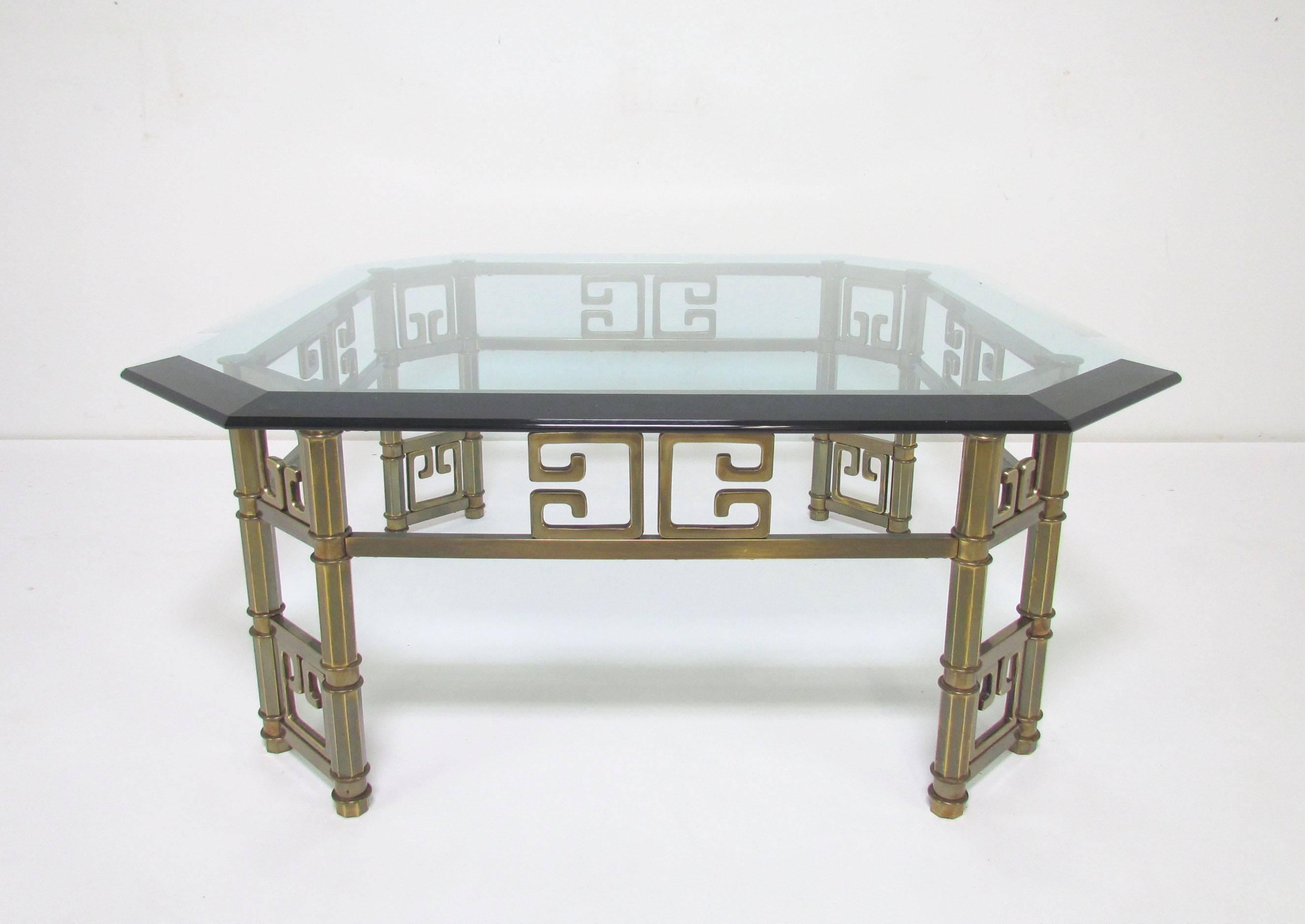 Substantial Mastercraft coffee table in brass with a decorative Greek key motif, canted legs support a thick beveled octagonal glass top.