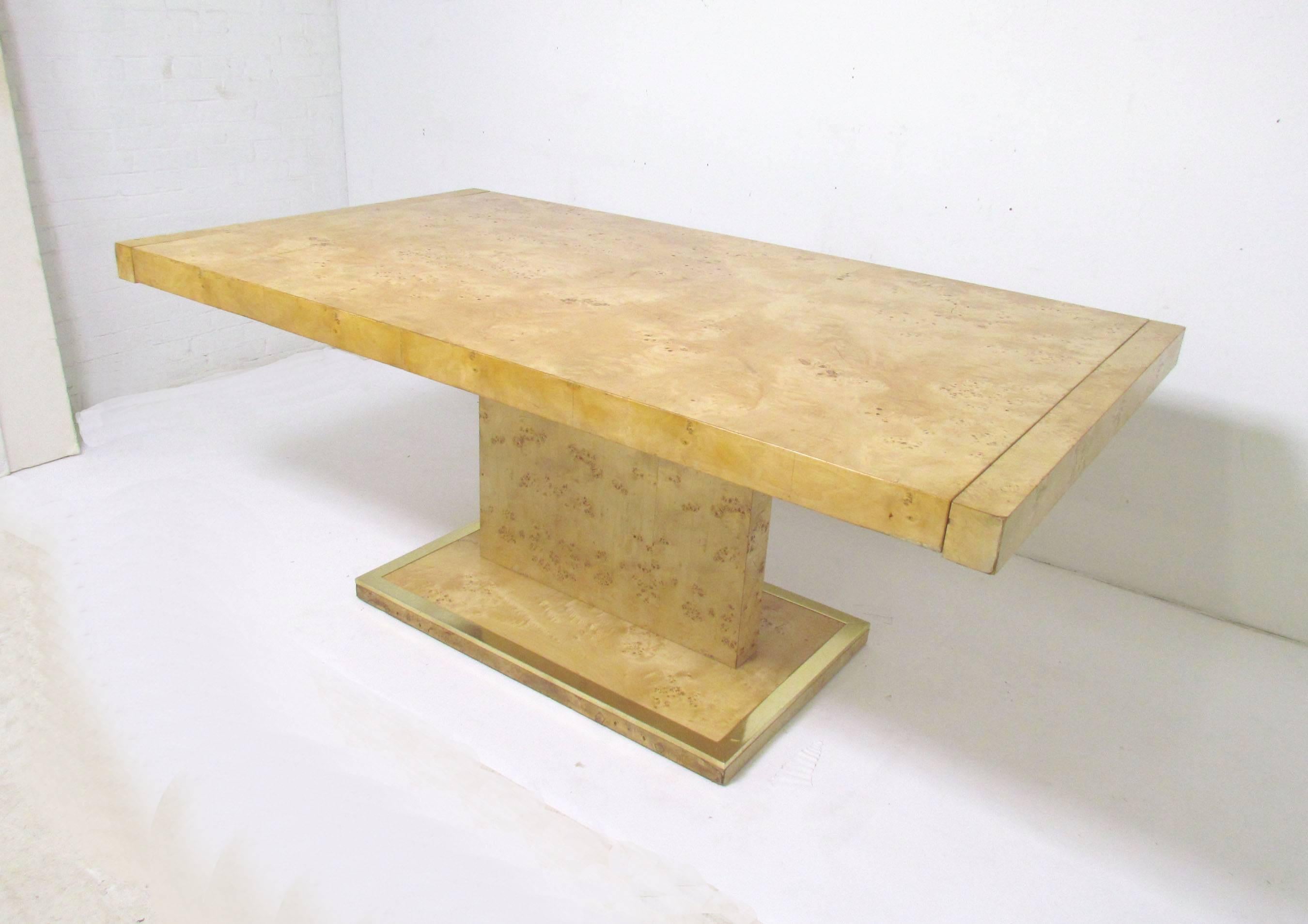 Impressive pedestal form Mid-Century Modern burl wood dining table by Founders, a division of Thomasville Furniture, circa 1970s, in the manner of Milo Baughman. Features brass accented pedestal base, and two extension leaves that drop into either