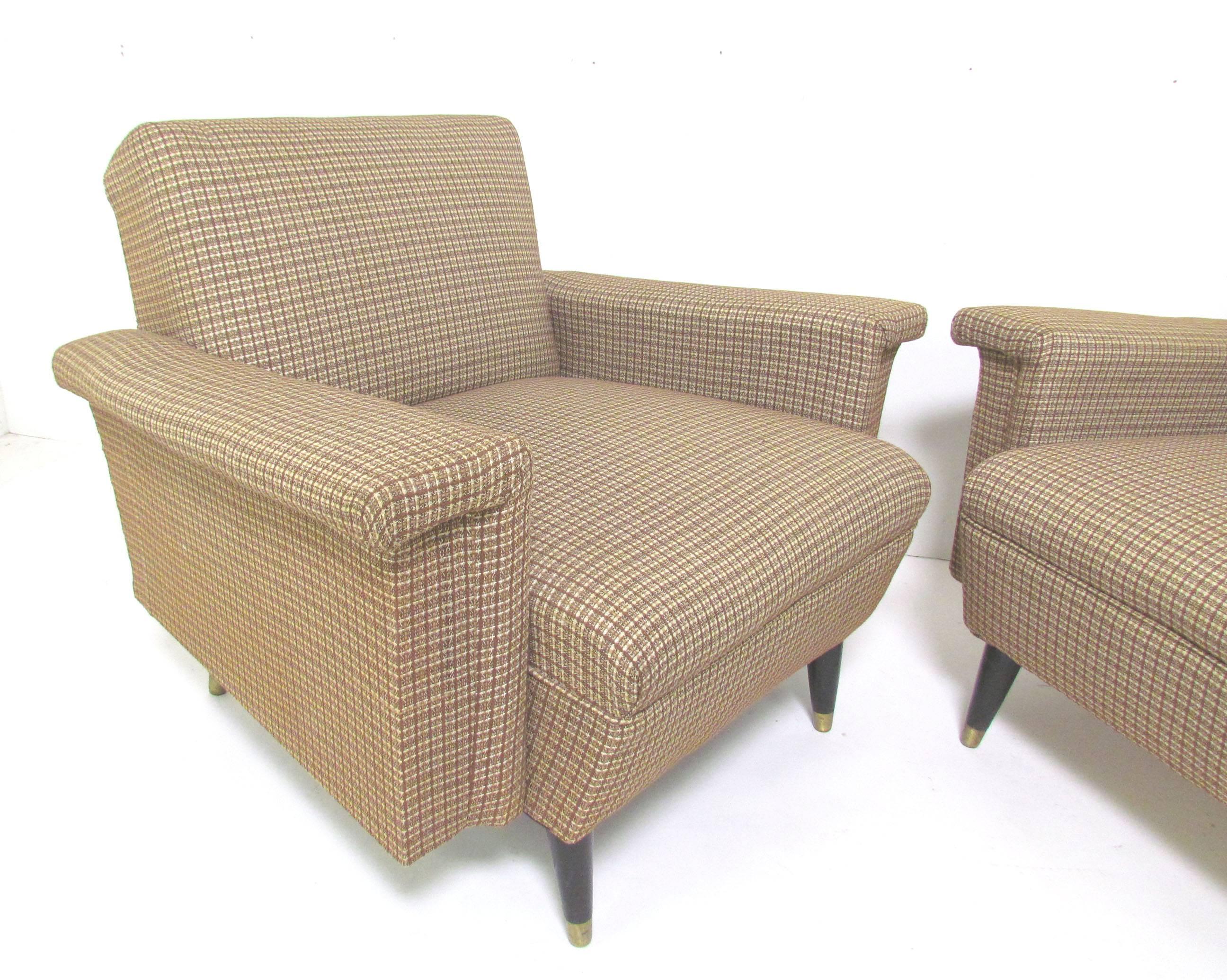Pair of mid-century modern club lounge chairs with unusual upholstered boxed paddle arms, circa 1960s, with  gently splayed legs of ebonized wood with brass sabots.  These chairs echo the uniquely American avionic style of the late 1950s and early