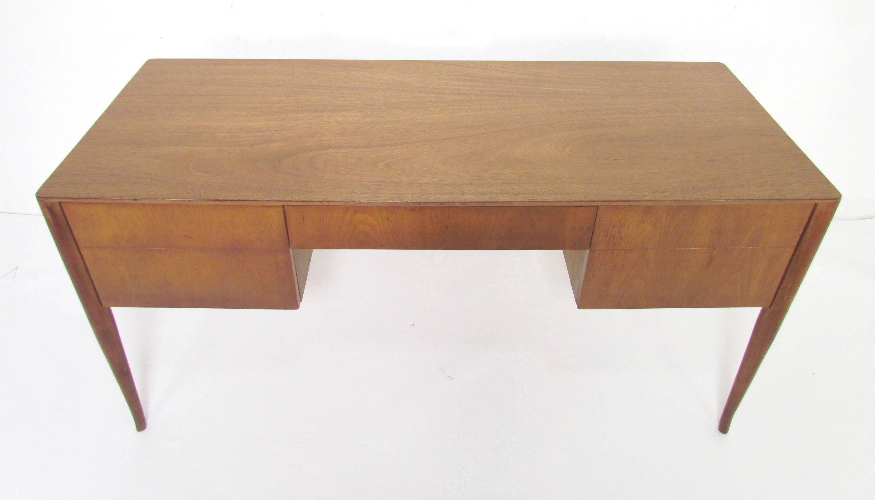 Sensuous writing desk with tapered saber legs by T.H. Robsjohn-Gibbings for Widdicomb, circa 1950s. Two flanking drawers on either side of center pencil drawer. Finished back allows this desk to float in a room or serve as a reception desk.