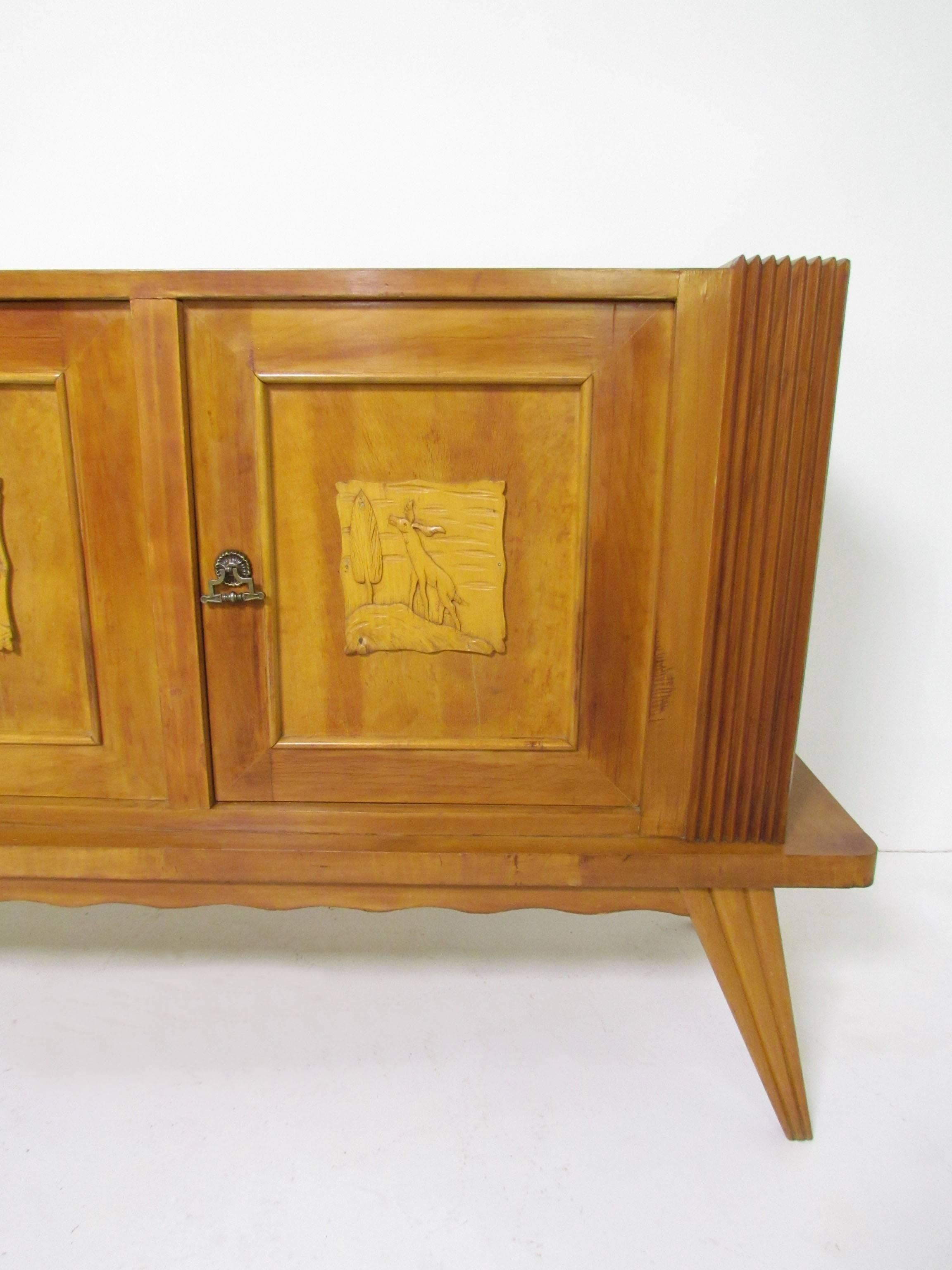 Unusual rustic sideboard, made in Italy, circa late 1940s-early 1950s. Hand-carved decorative panels on the door fronts, brass hardware, This wonderful hand built cabinet highlights its post war design with flared legs and radiant end fins atop an