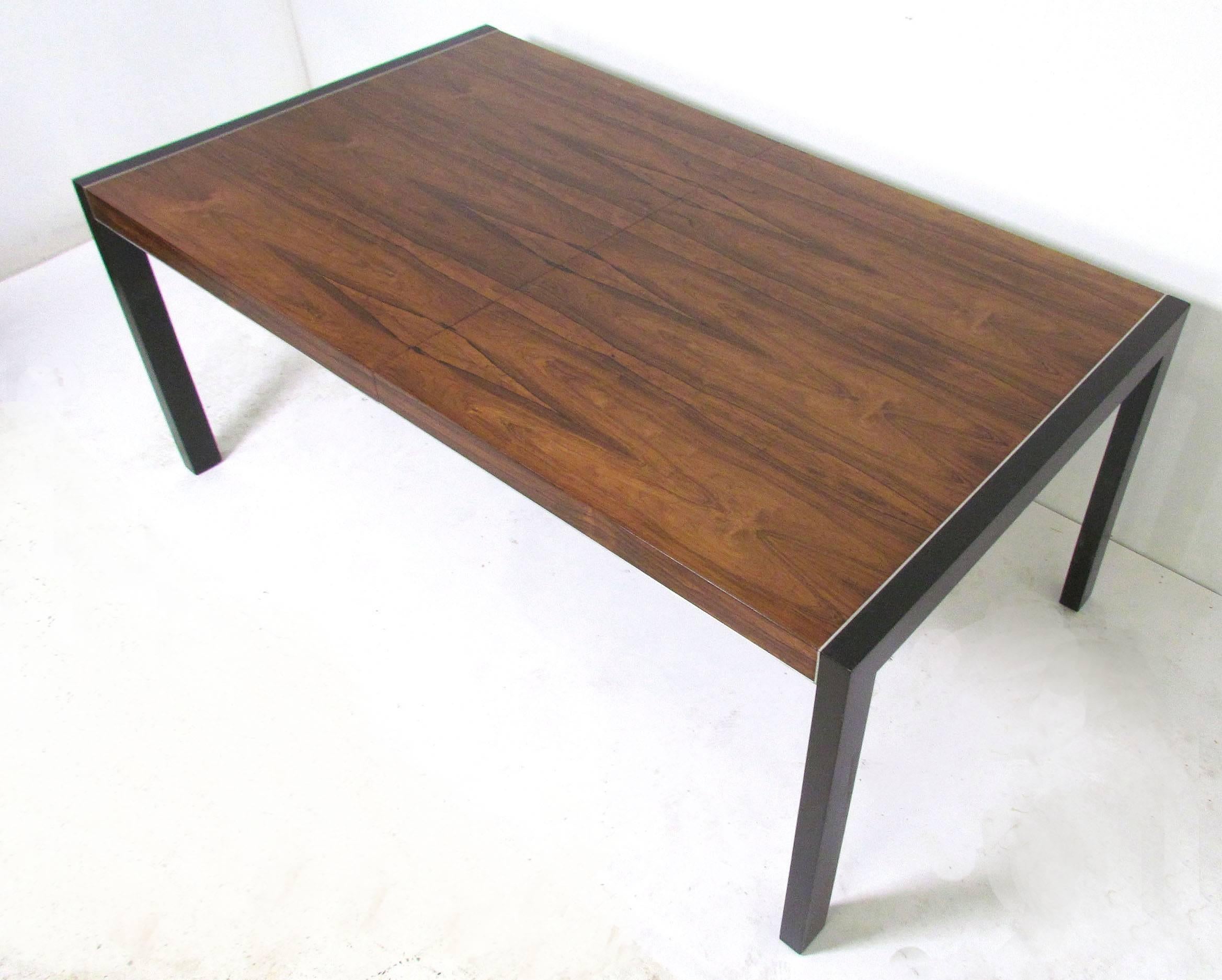 Mid-Century rosewood dining table with ebonized legs and aluminium trim, designed by Robert Baron for Glenn of California, circa 1960s. Includes two bookmatched 20
