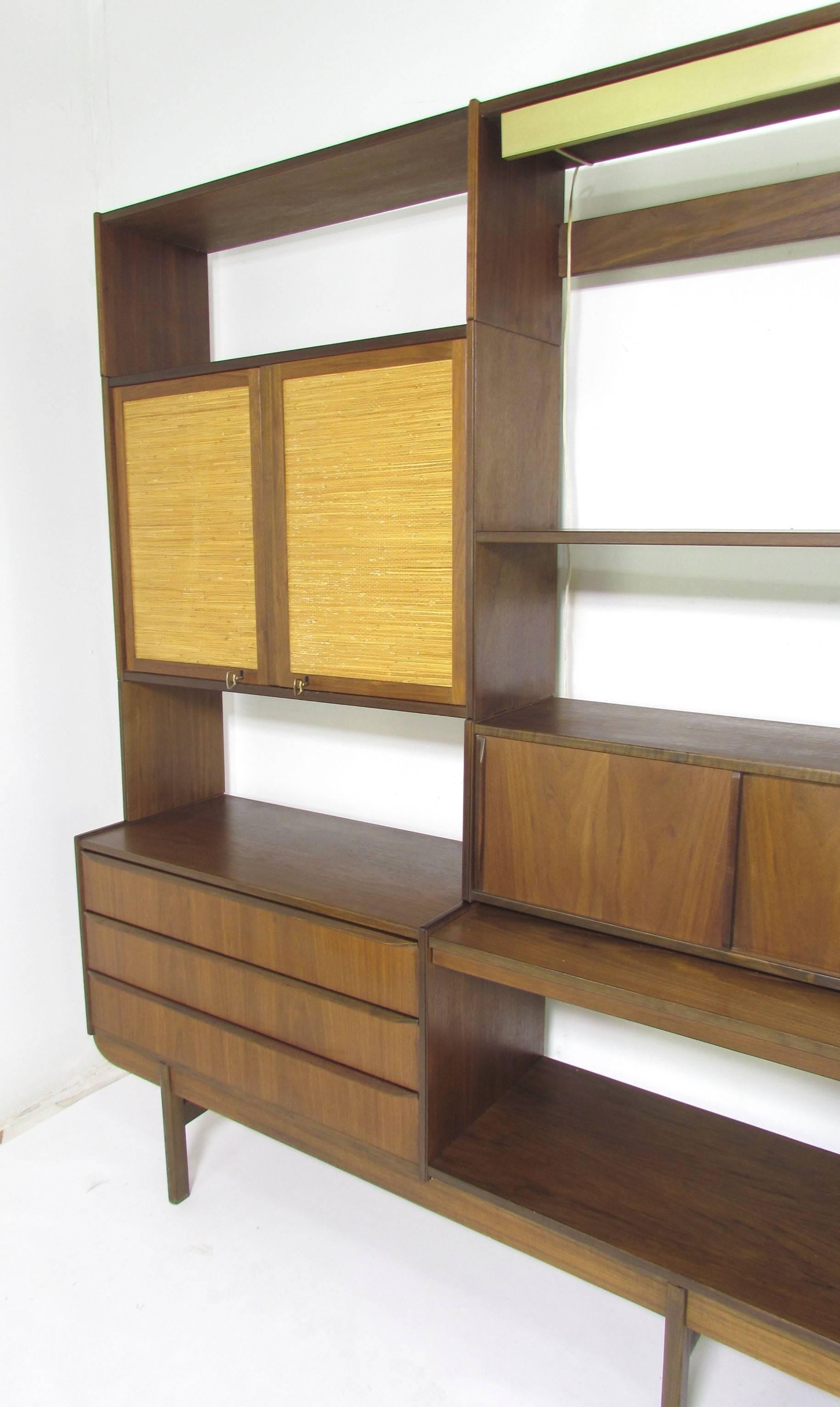 Large four bay freestanding wall unit, circa 1960s. Various drawers and storage compartments, and a pull-out writing desk surface. Mounted with an overhead Lightolier fixture. Four original keys for the cane-front cabinets.